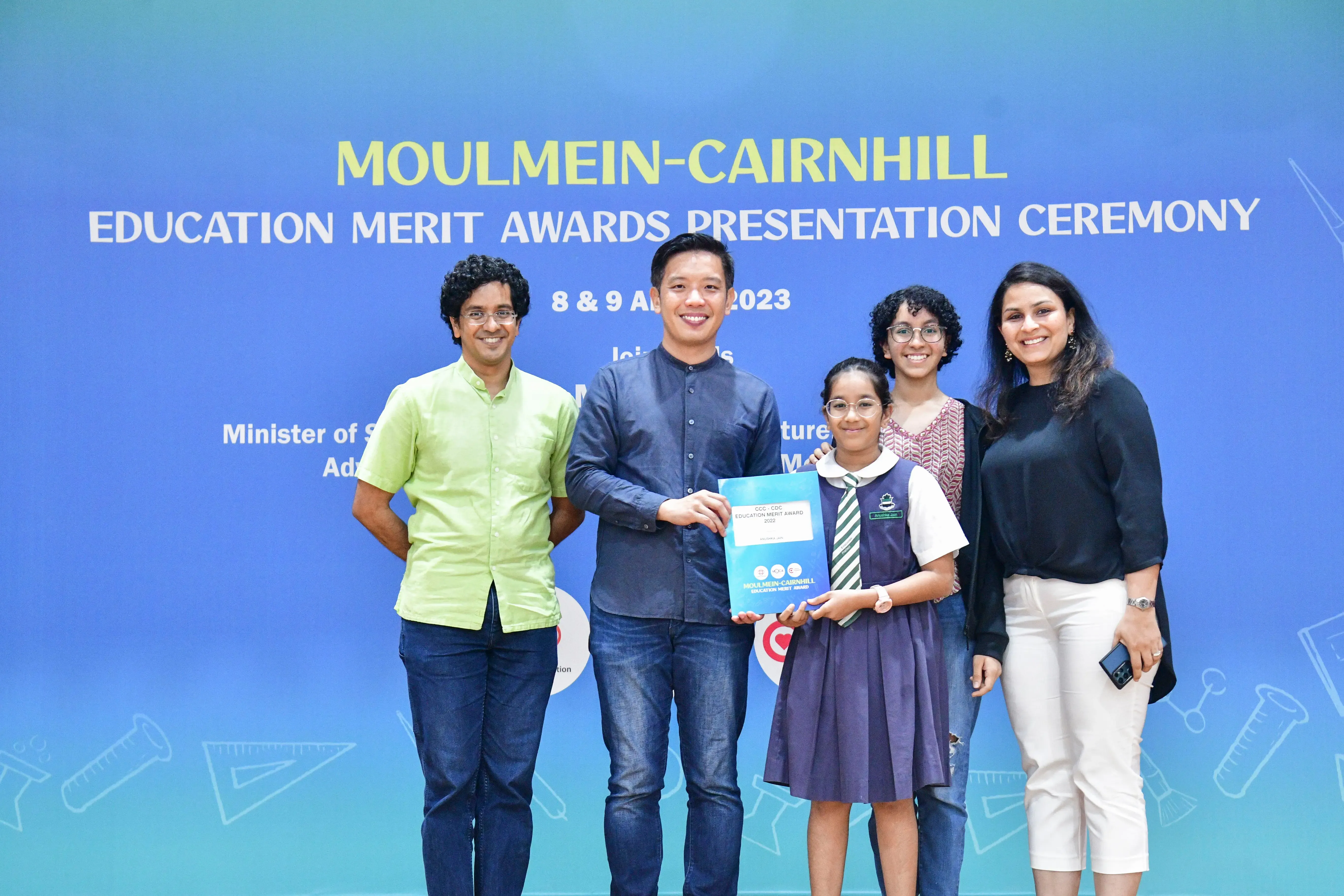 Four adults and a young girl in school uniform pose at the Moulmein-Cairnhill Education Merit Awards 2023.