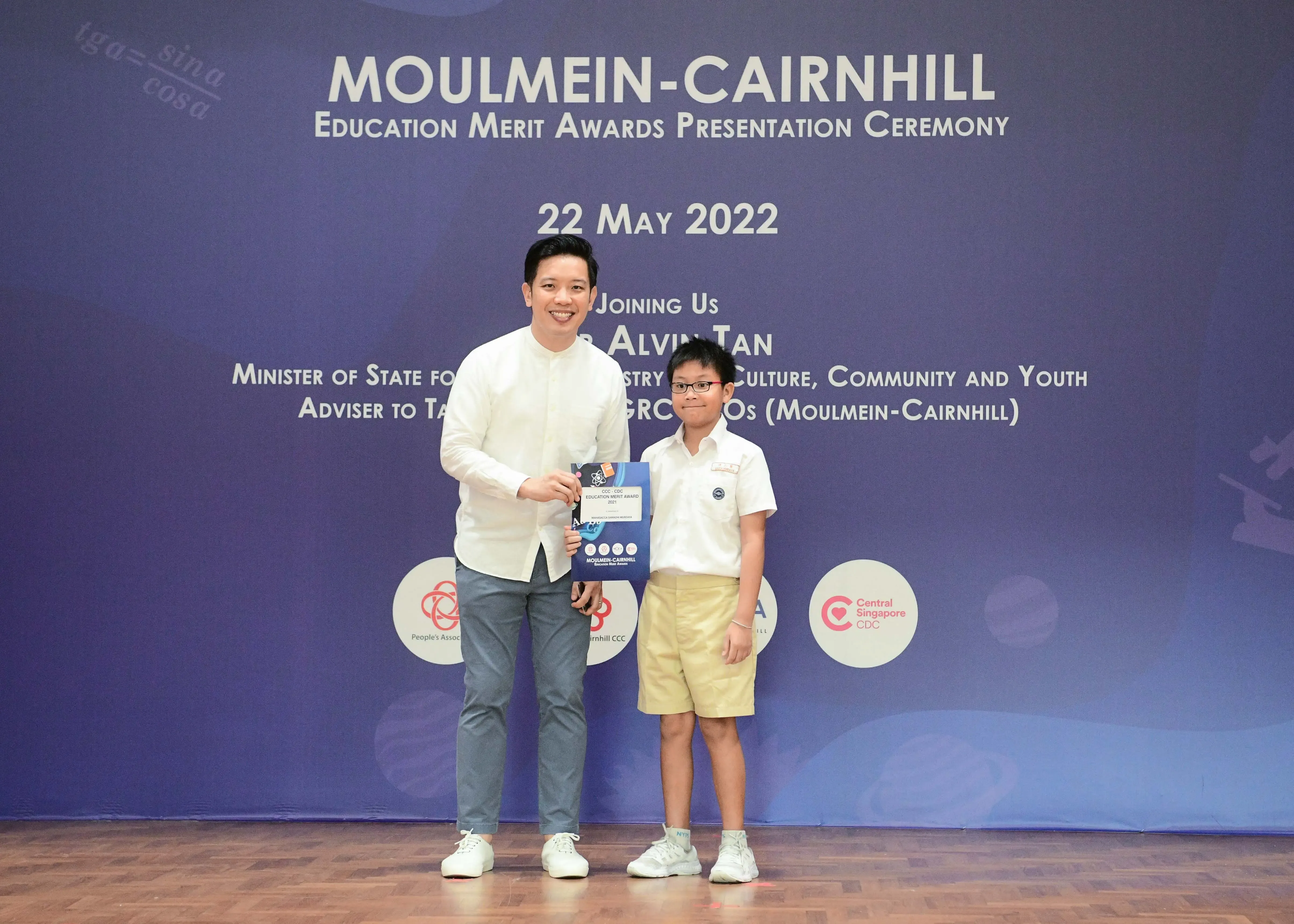 A man and a young boy in school uniform hold a certificate at the Moulmein-Cairnhill Education Merit Awards on 22 May 2022.