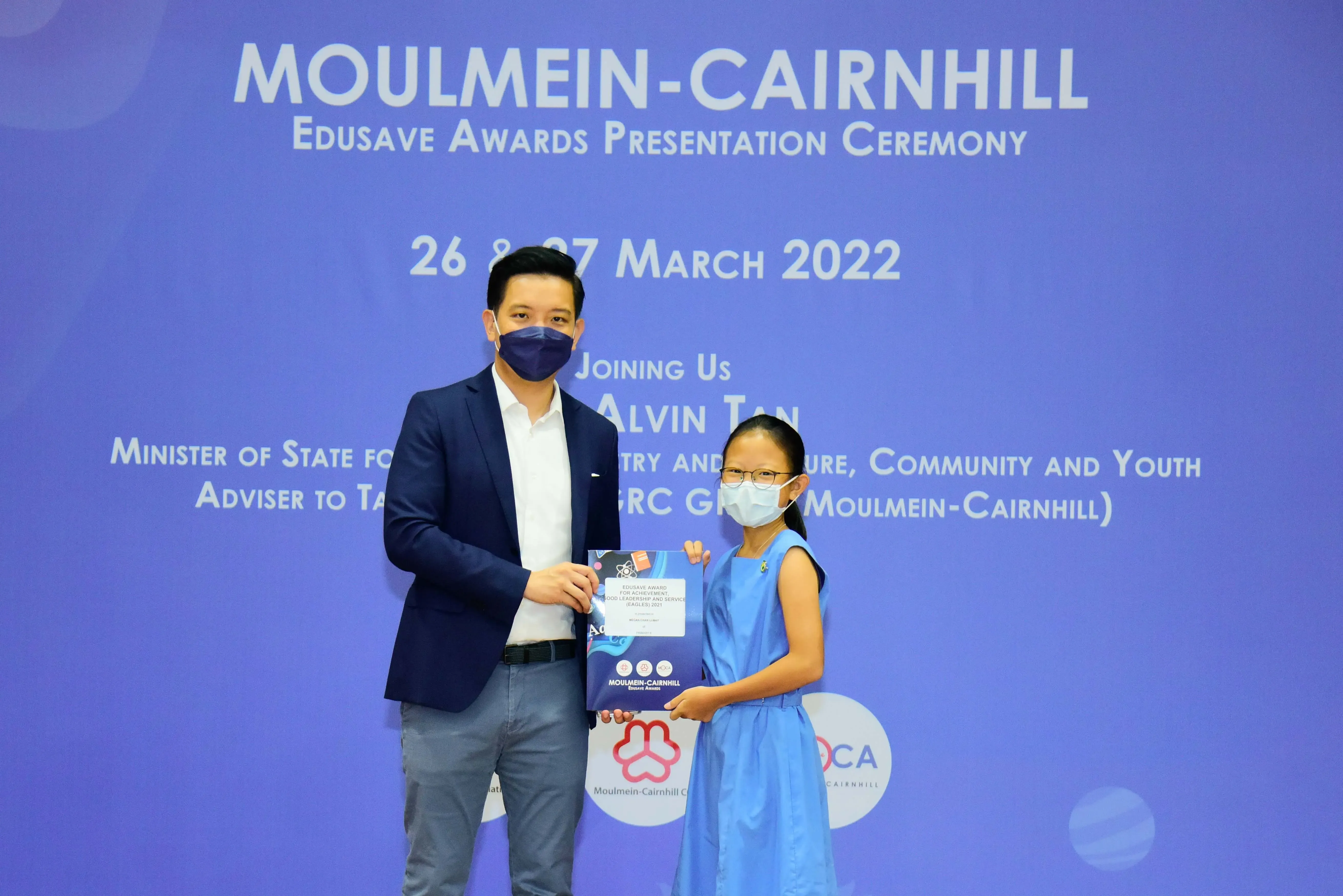 A man and a young girl hold an award together at the Moulmein-Cairnhill Edusave Awards Ceremony, March 2022.