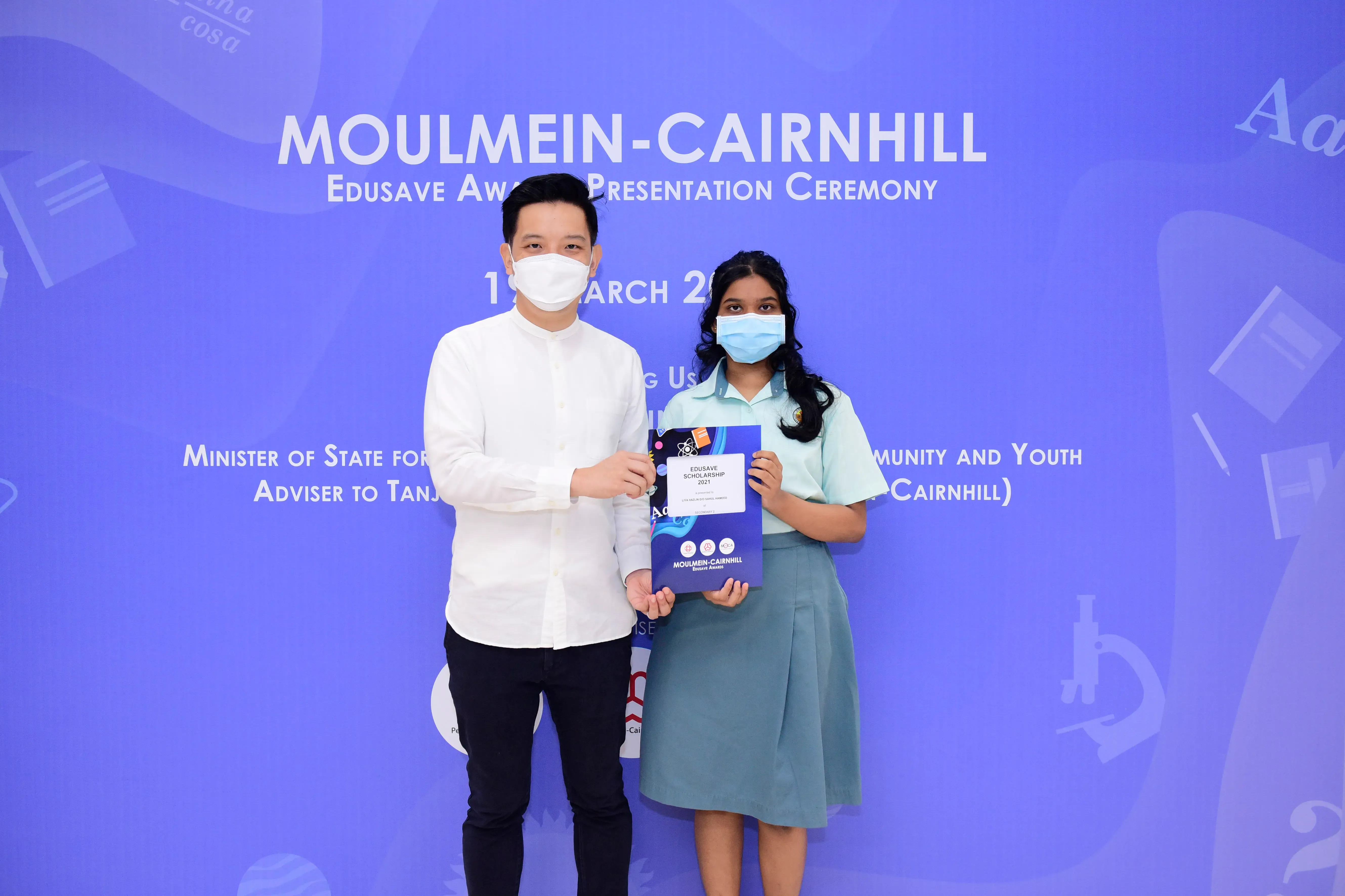 Two masked people holding an Edusave Scholarship certificate at the Moulmein-Cairnhill Award Presentation Ceremony.