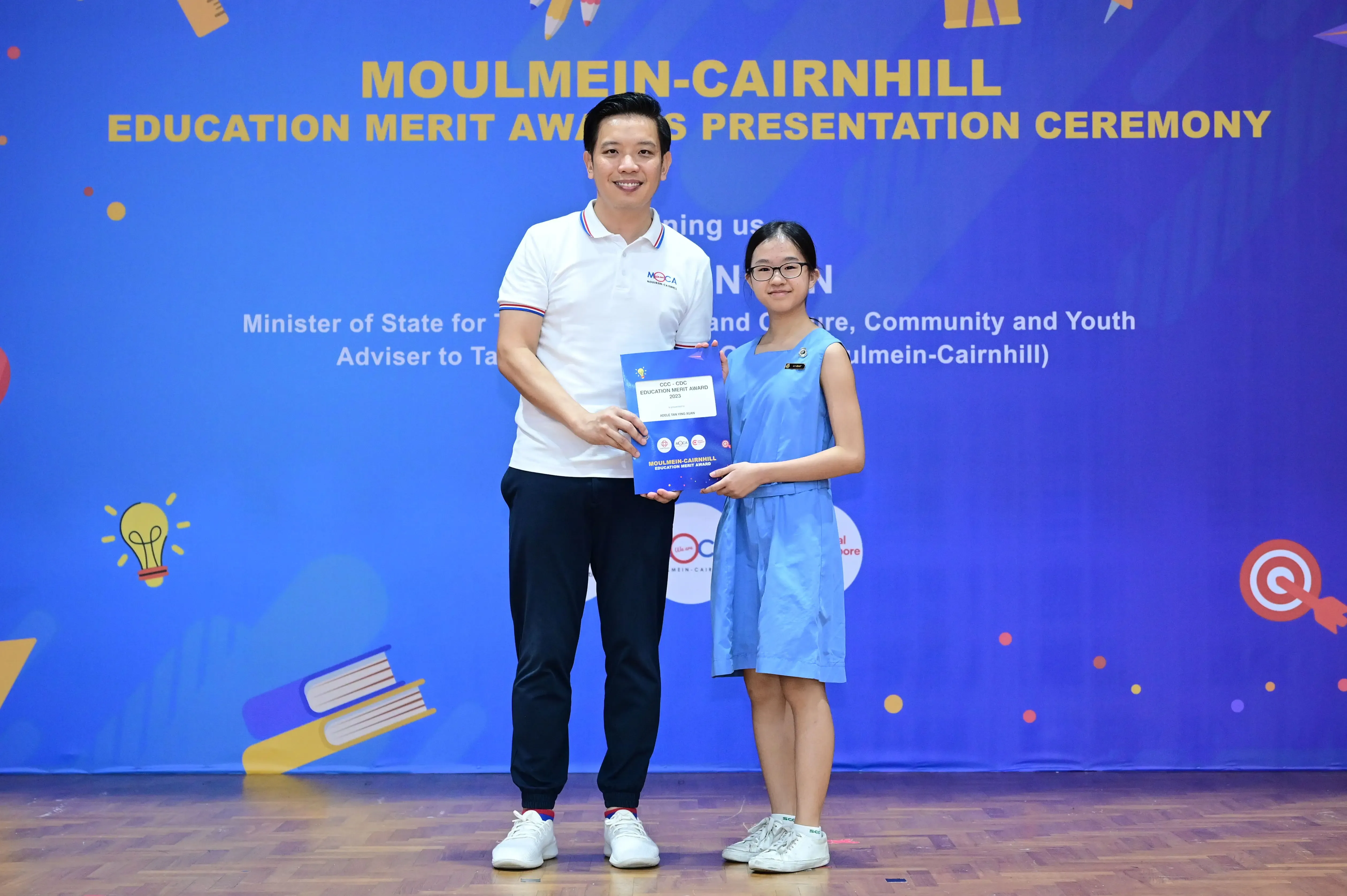Man and young girl holding an award booklet at the Moulmein-Cairnhill Education Merit Awards Presentation Ceremony.