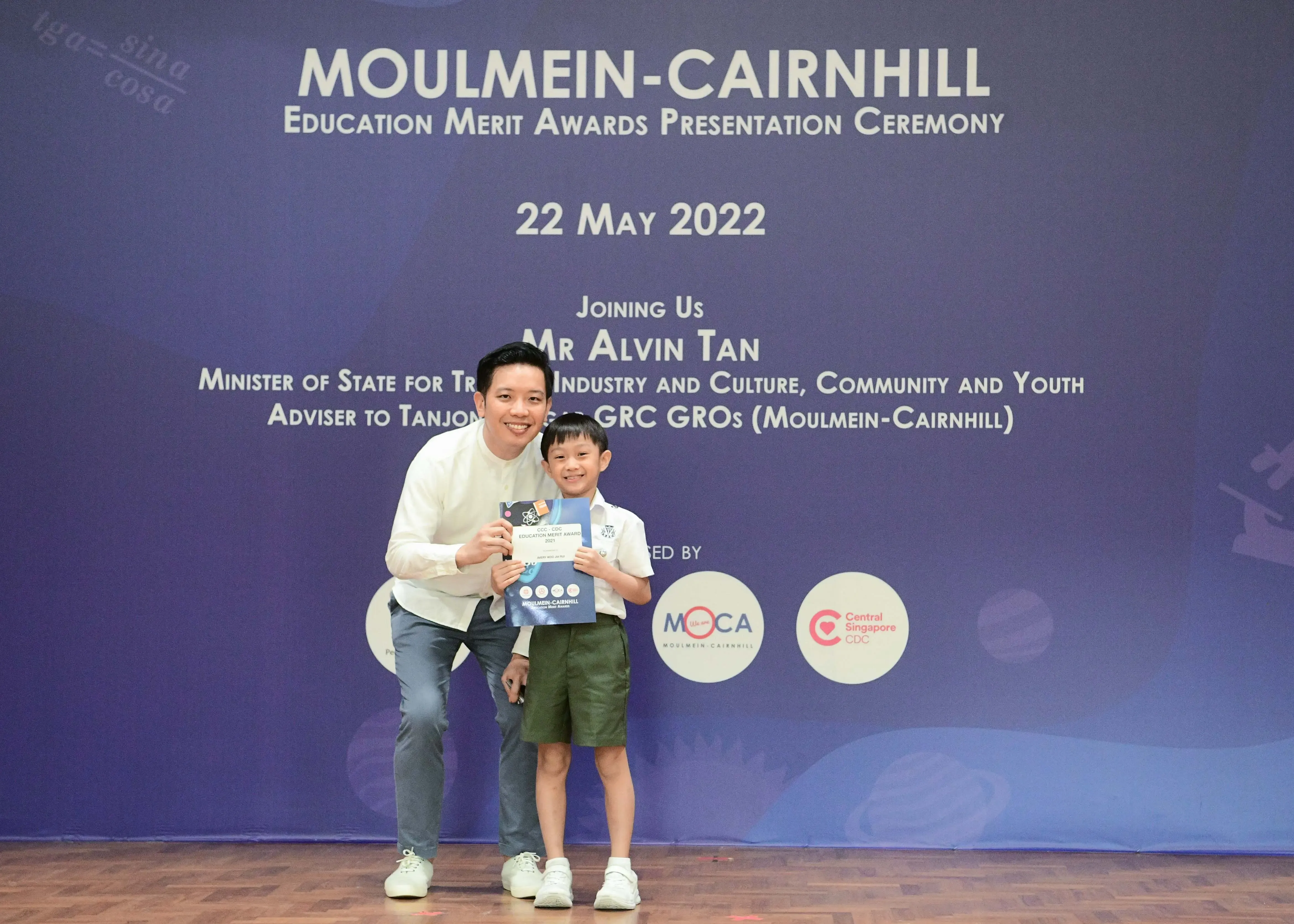 A man and a young boy pose together holding an award certificate at the Moulmein-Cairnhill Education Merit Awards ceremony.