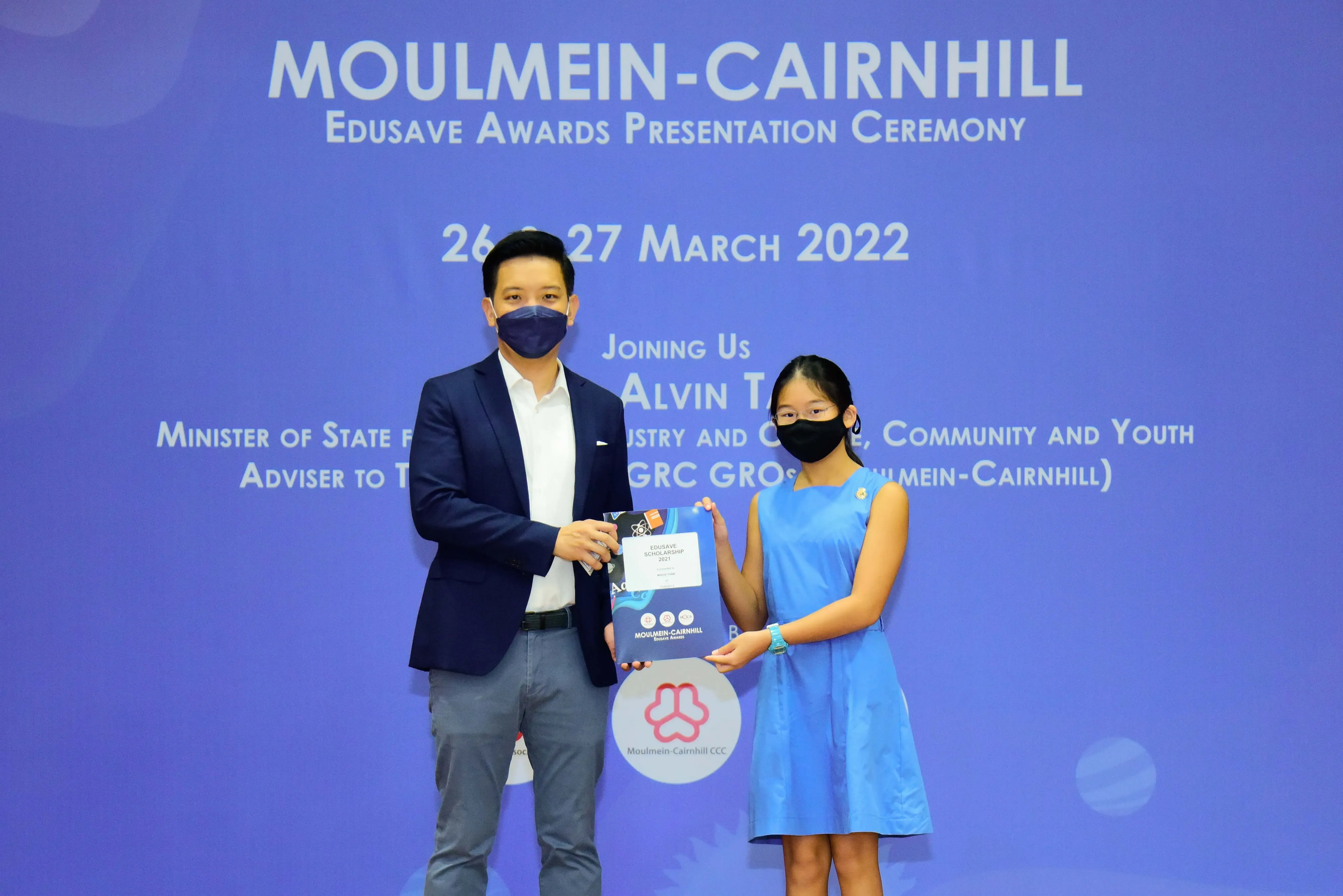 A man and a young girl wearing masks hold an award at the Moulmein-Cairnhill Edusave Awards Ceremony, March 2022.