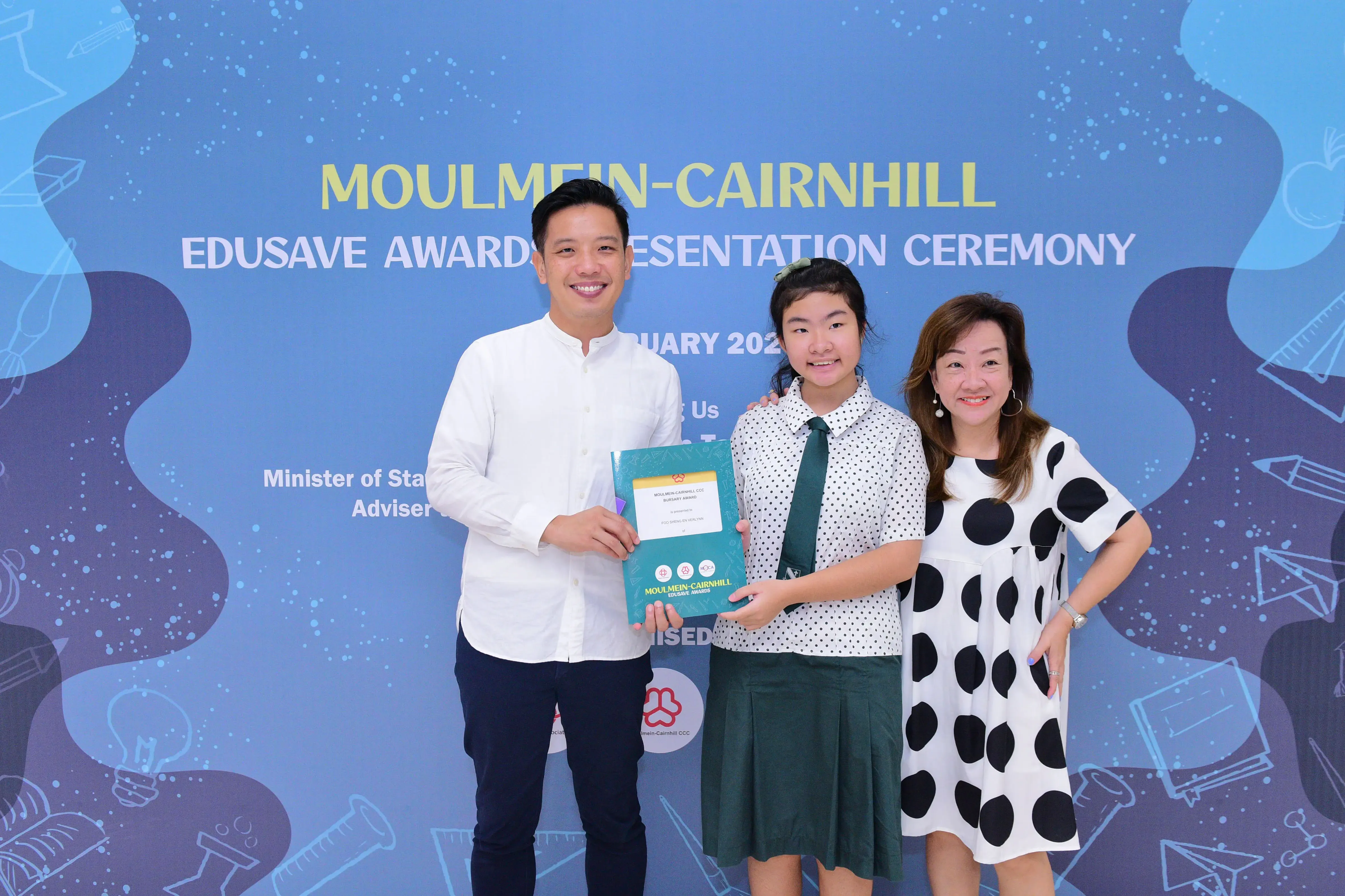 Three people smile and hold an award folder at the Moulmein-Cairnhill Edusave Awards Presentation Ceremony.