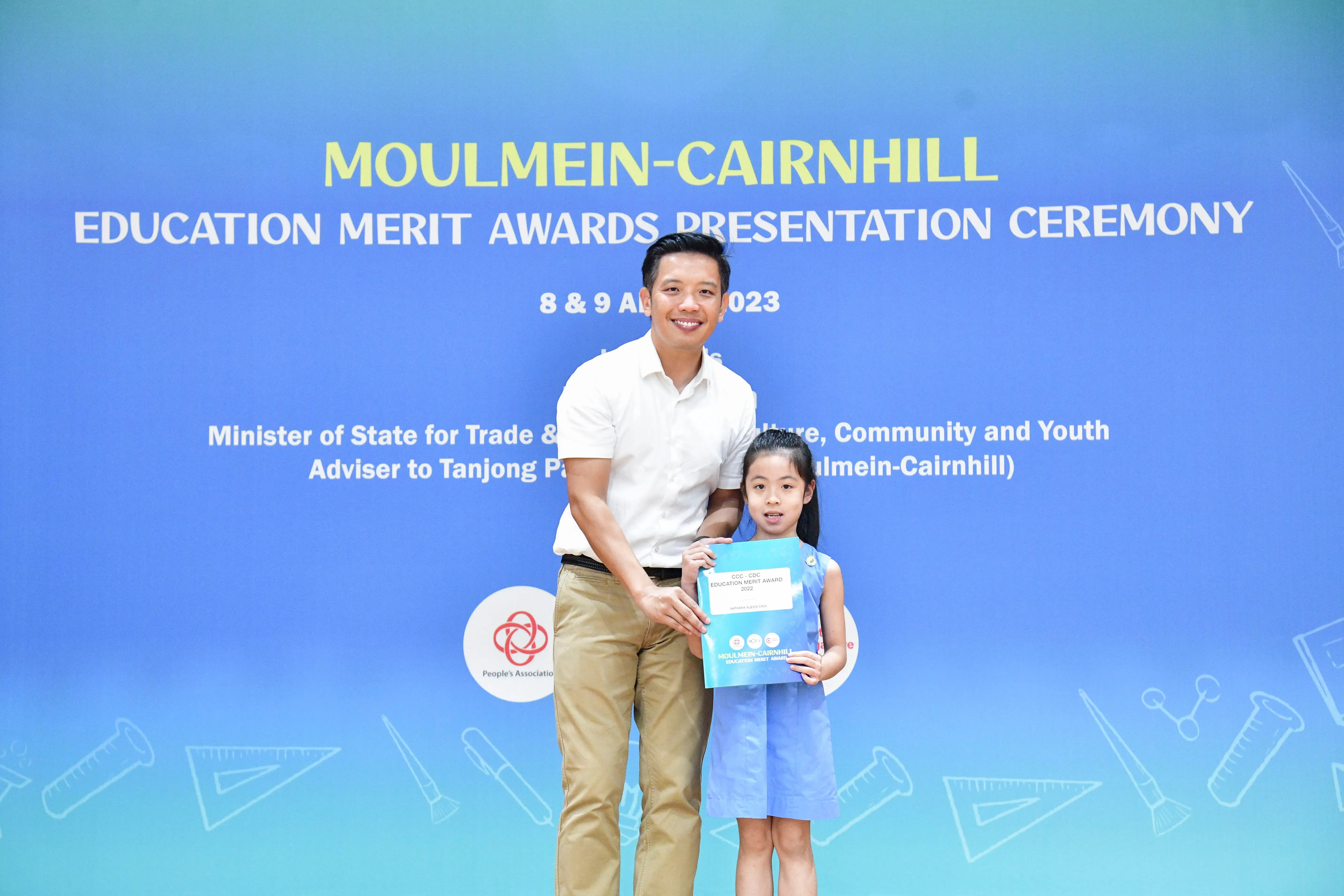 A man and a young girl hold an award certificate at the Moulmein-Cairnhill Education Merit Awards Ceremony 2023.