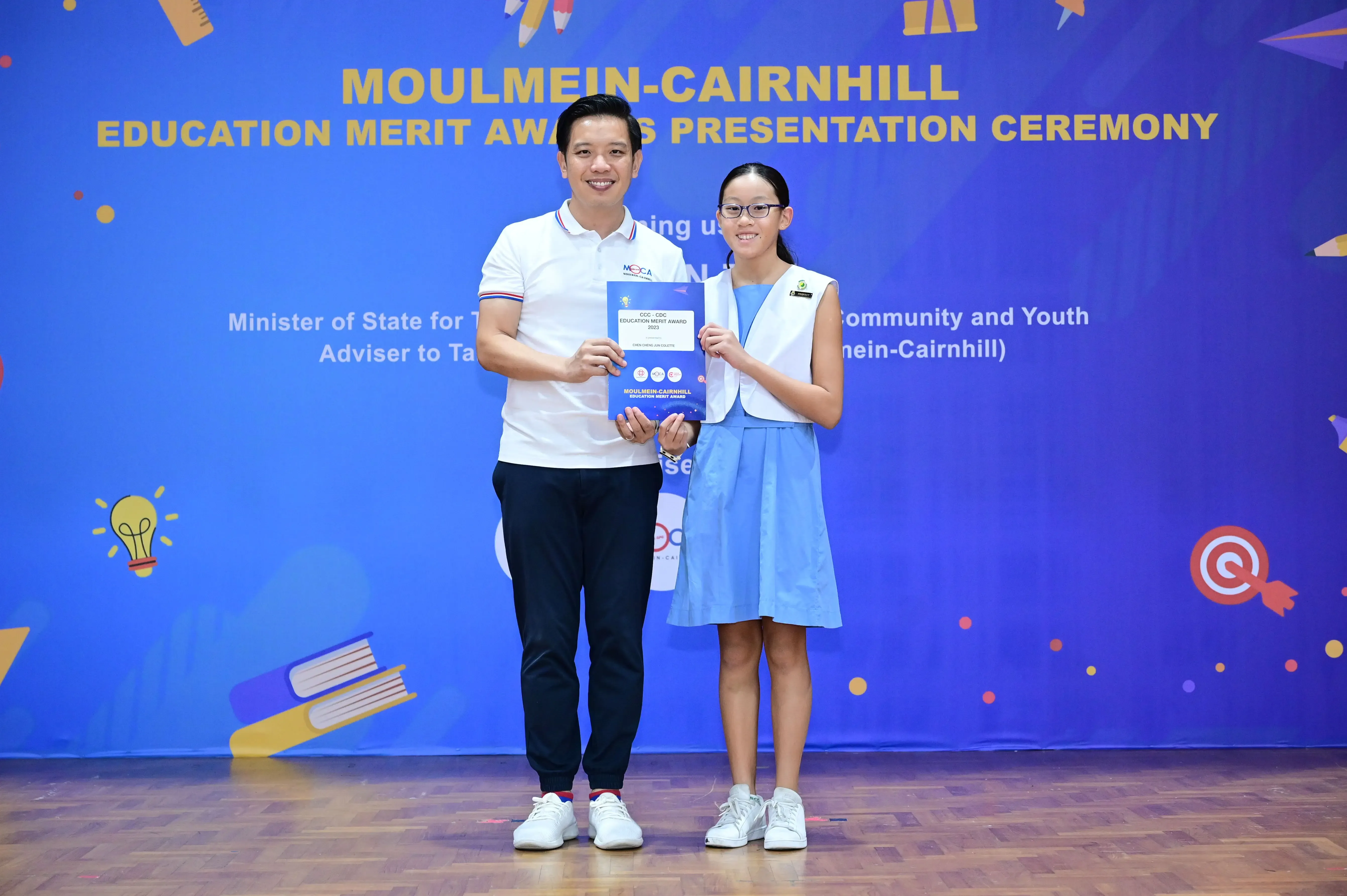 A man and a young girl hold an award certificate at the Moulmein-Cairnhill Education Merit Awards Presentation Ceremony.