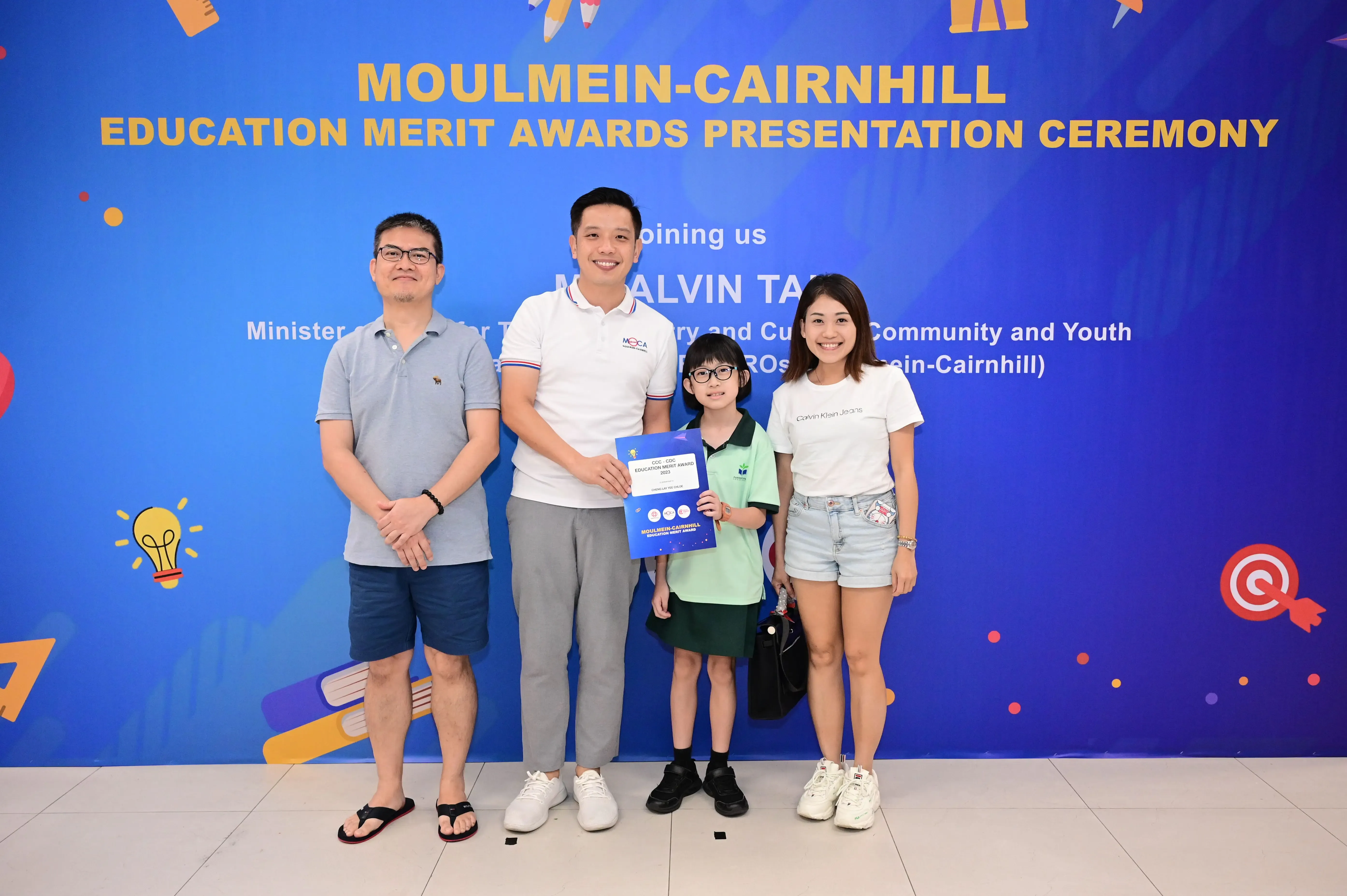 Three adults and a child pose with a certificate at the Moulmein-Cairnhill Education Merit Awards ceremony.