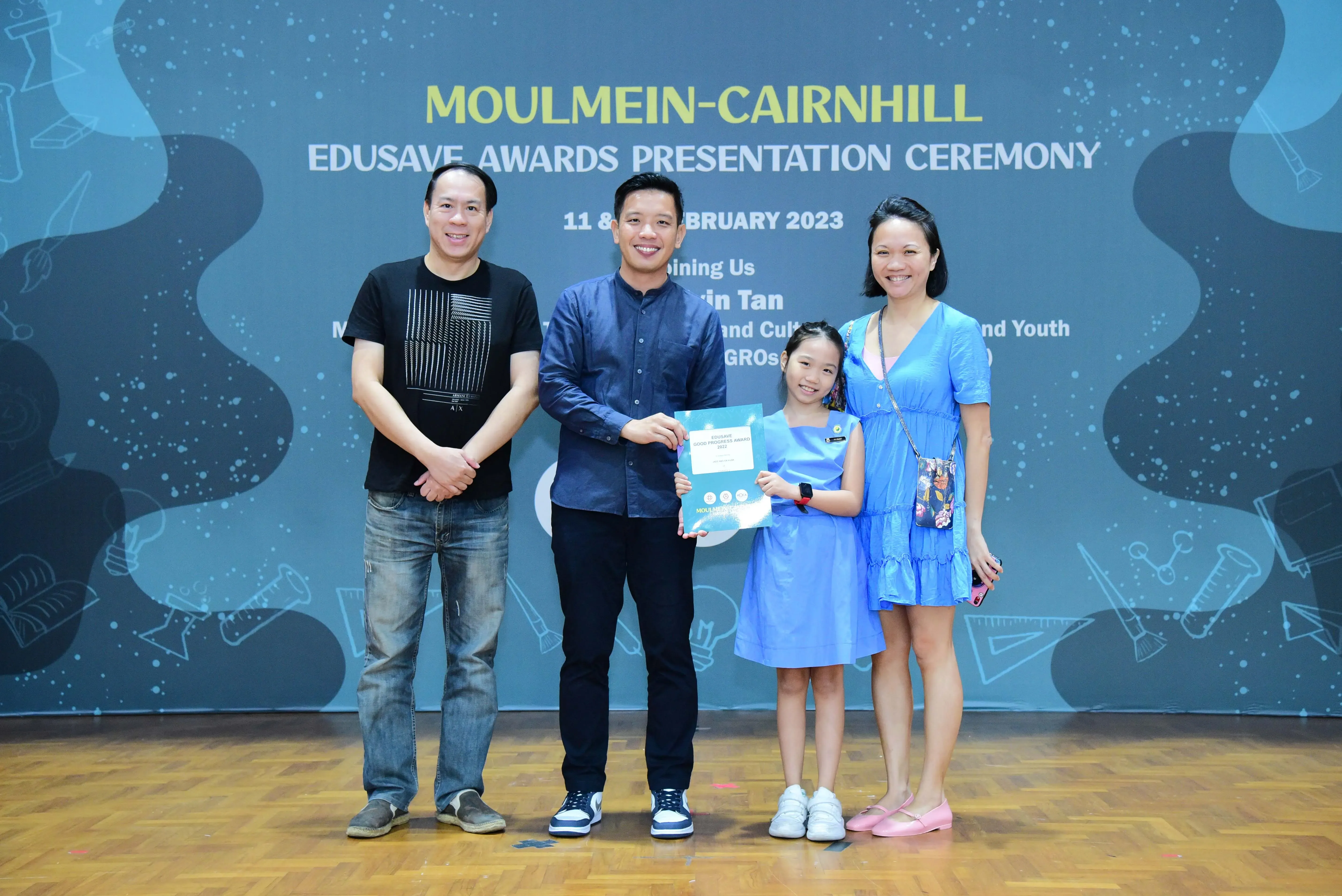 Four people pose at the Moulmein-Cairnhill Edusave Awards Presentation Ceremony in February 2023, with a girl holding a certificate.