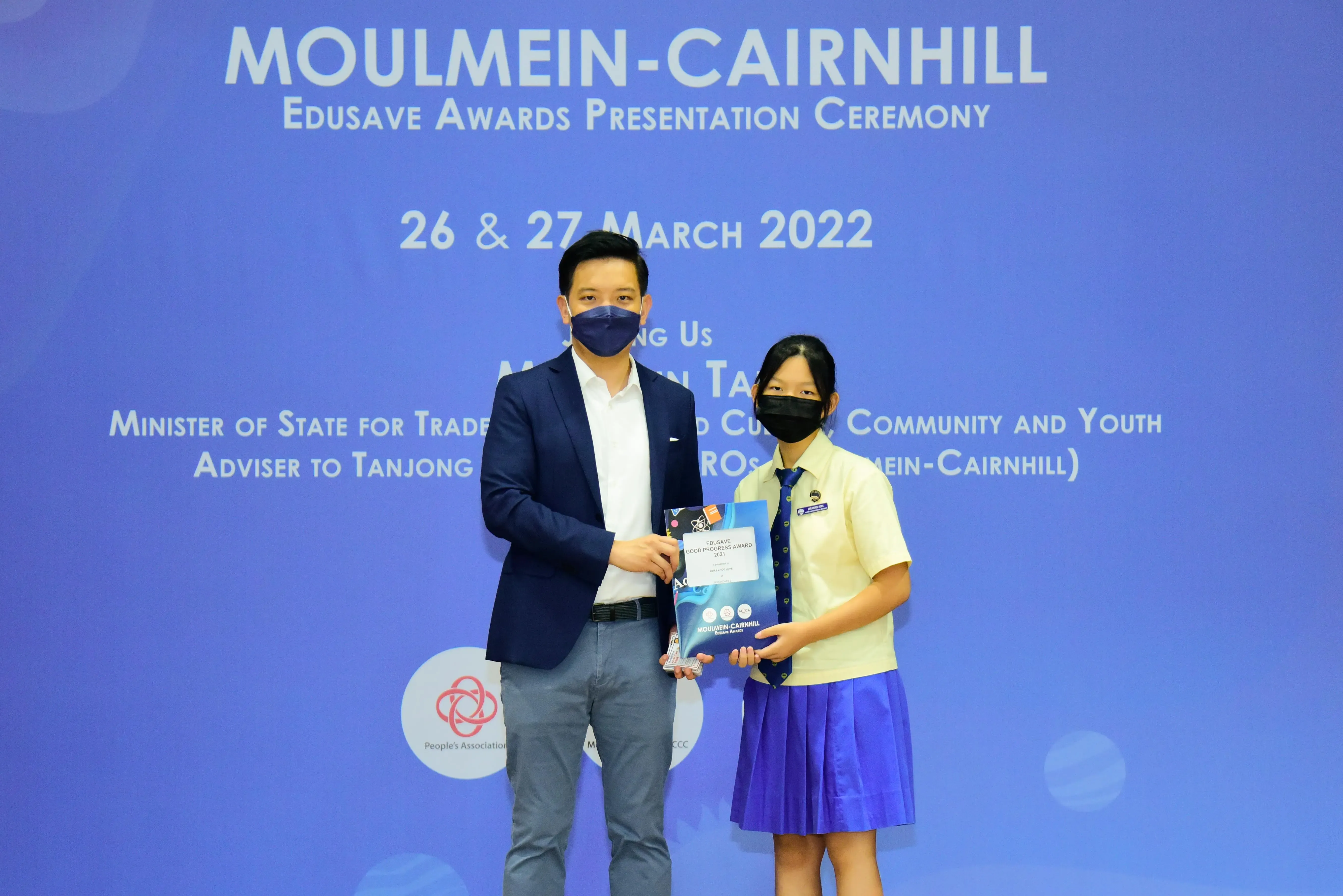 A masked man and a school girl hold an award at the Moulmein-Cairnhill Edusave Awards Ceremony, March 2022.