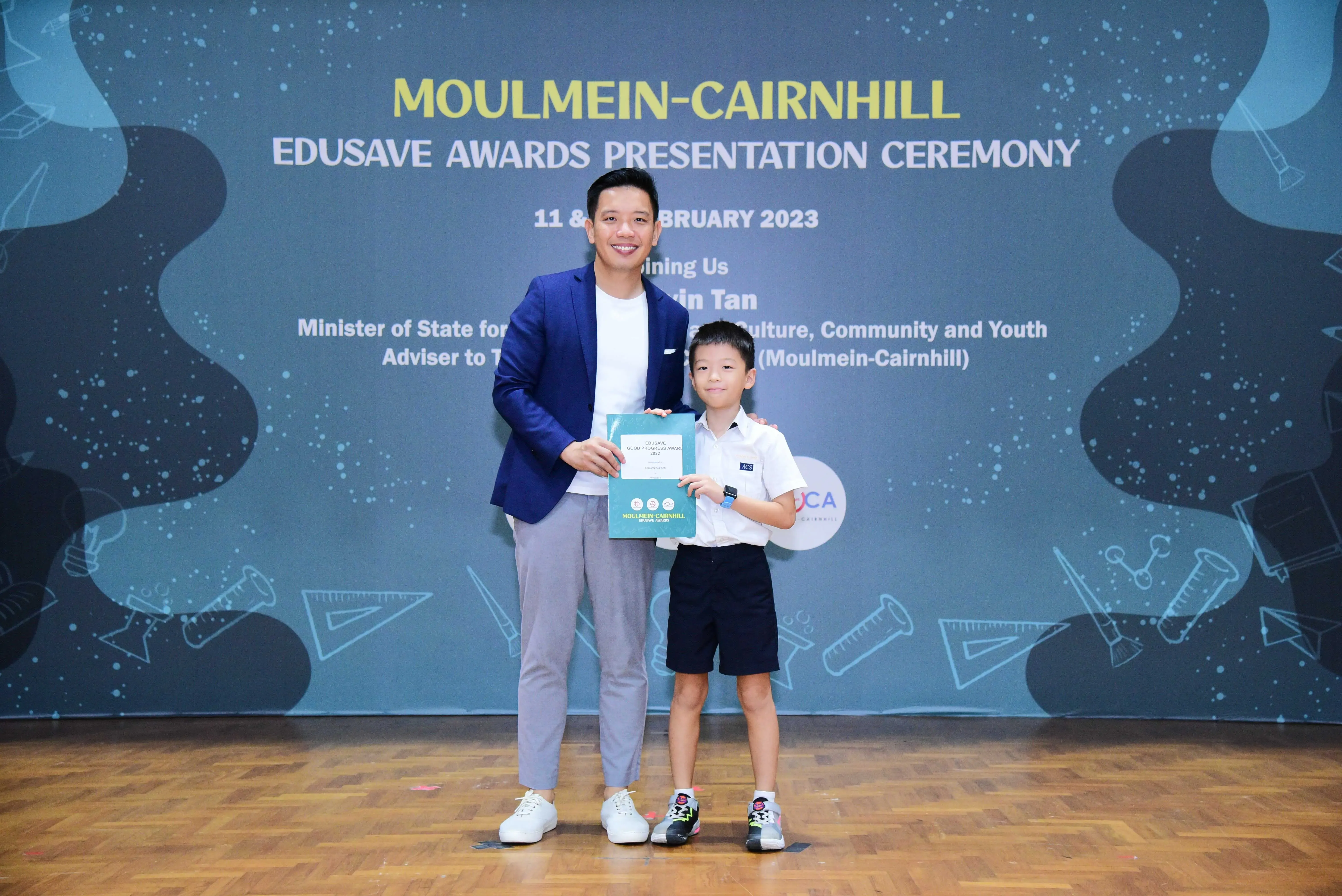 A man in a blue blazer and a young boy in school uniform hold a certificate at the Moulmein-Cairnhill Edusave Awards 2023.