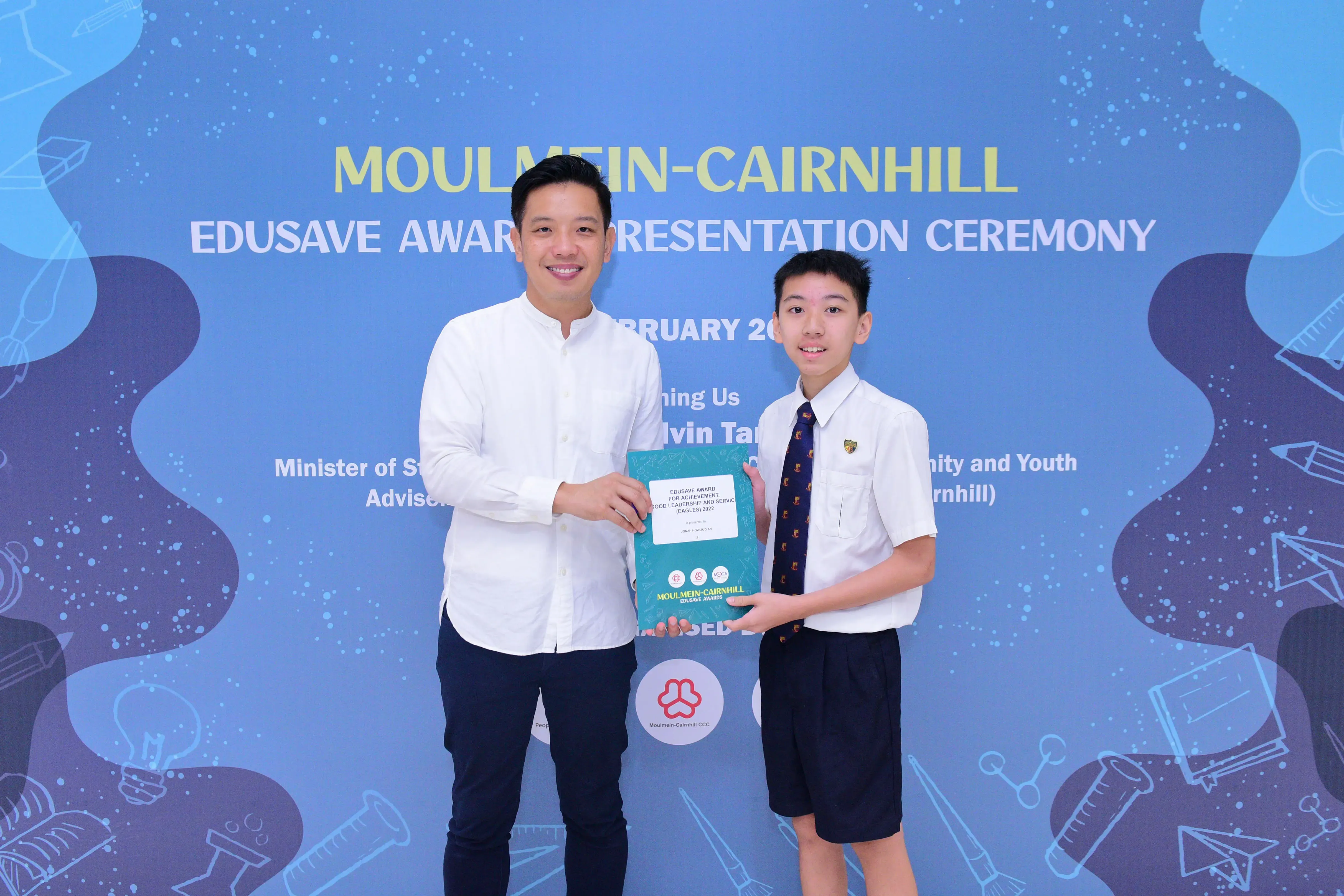 An adult and a uniformed student hold an award certificate at the Moulmein-Cairnhill Edusave Award Presentation Ceremony.