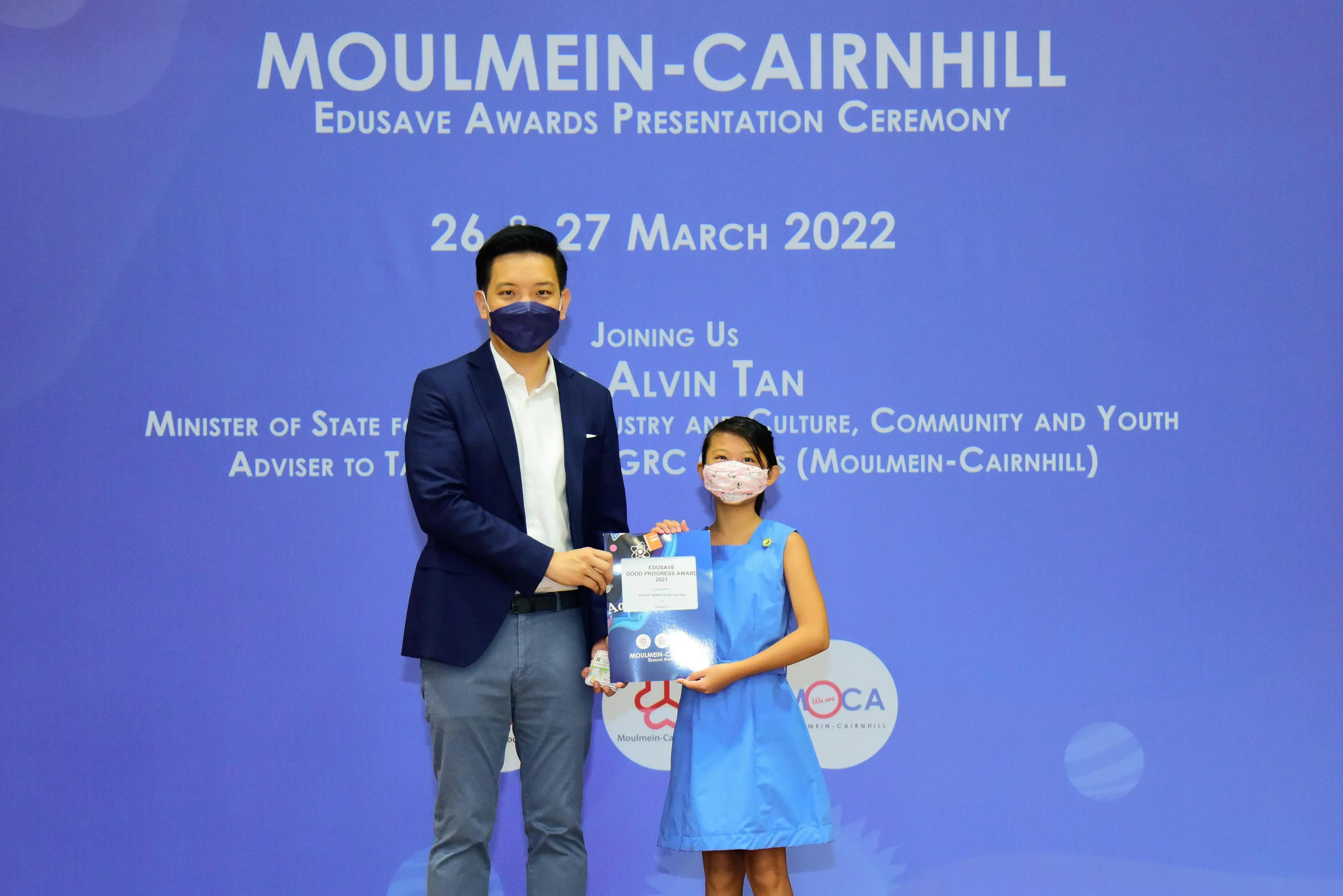 Man and young girl in masks hold an award at Moulmein-Cairnhill Edusave Awards Ceremony, March 2022.