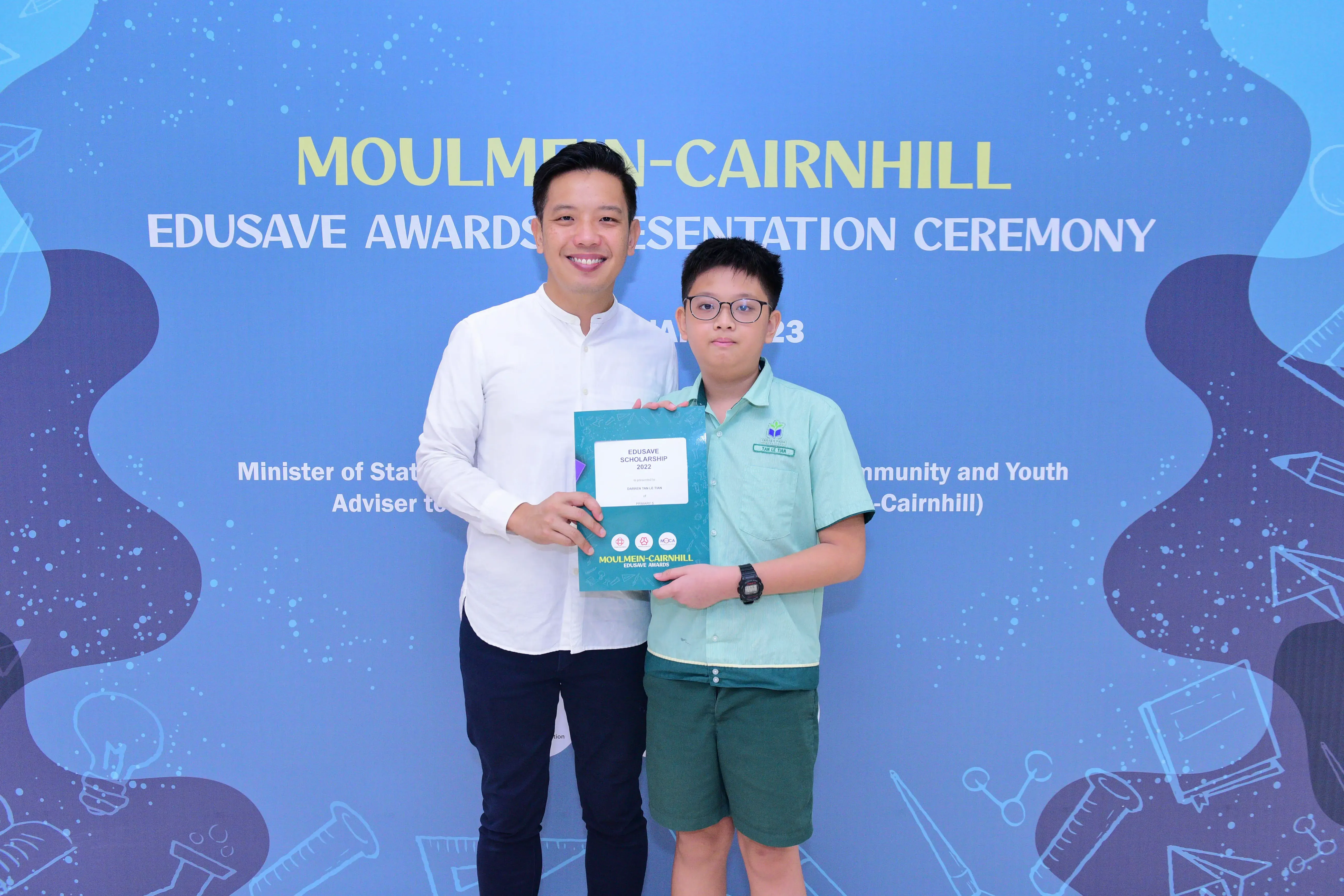 A man and a young boy holding an Edusave Scholarship certificate at the Moulmein-Cairnhill Awards Ceremony.