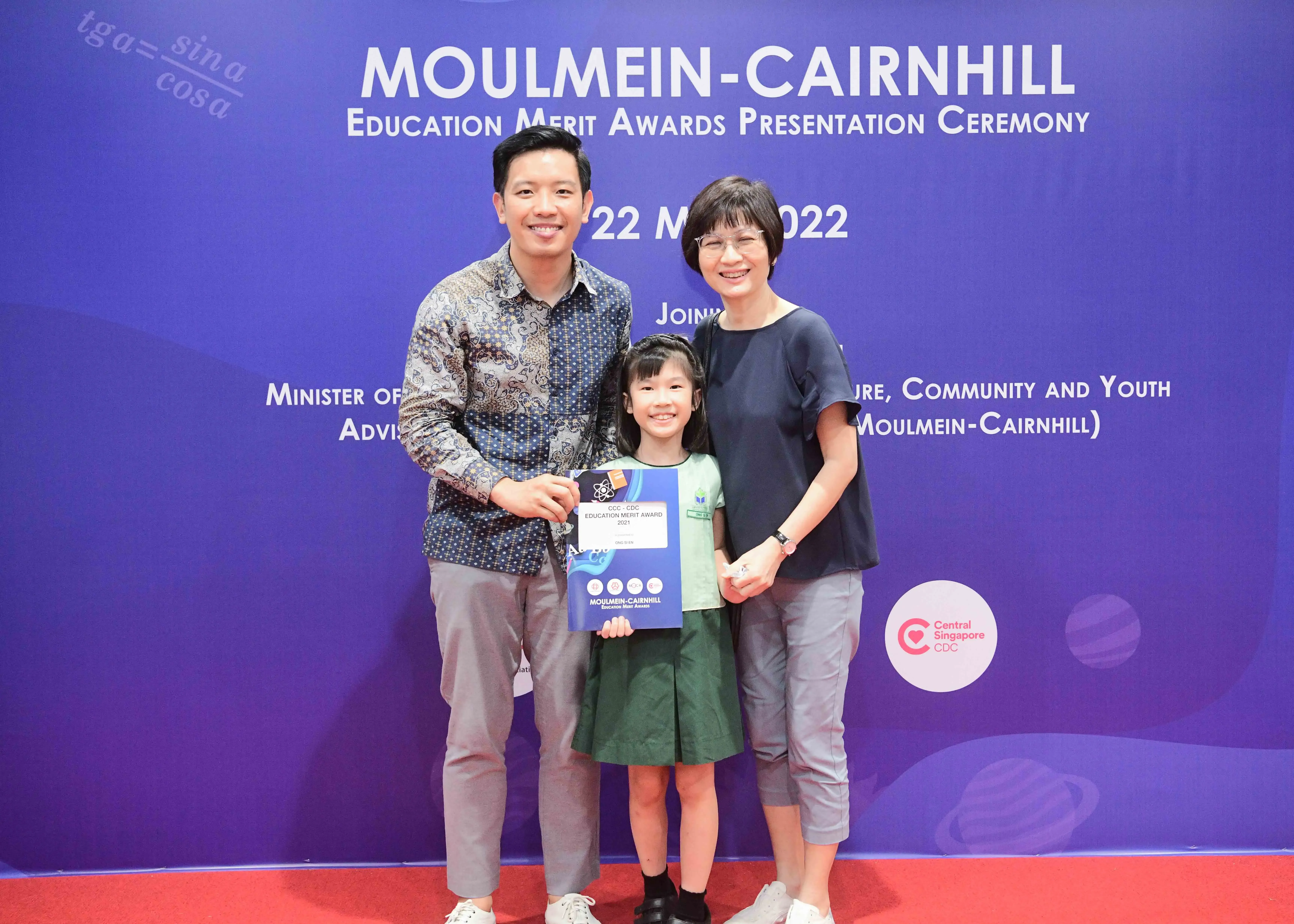 Two adults and a young girl holding an award certificate pose at the Moulmein-Cairnhill Education Merit Awards 2022.