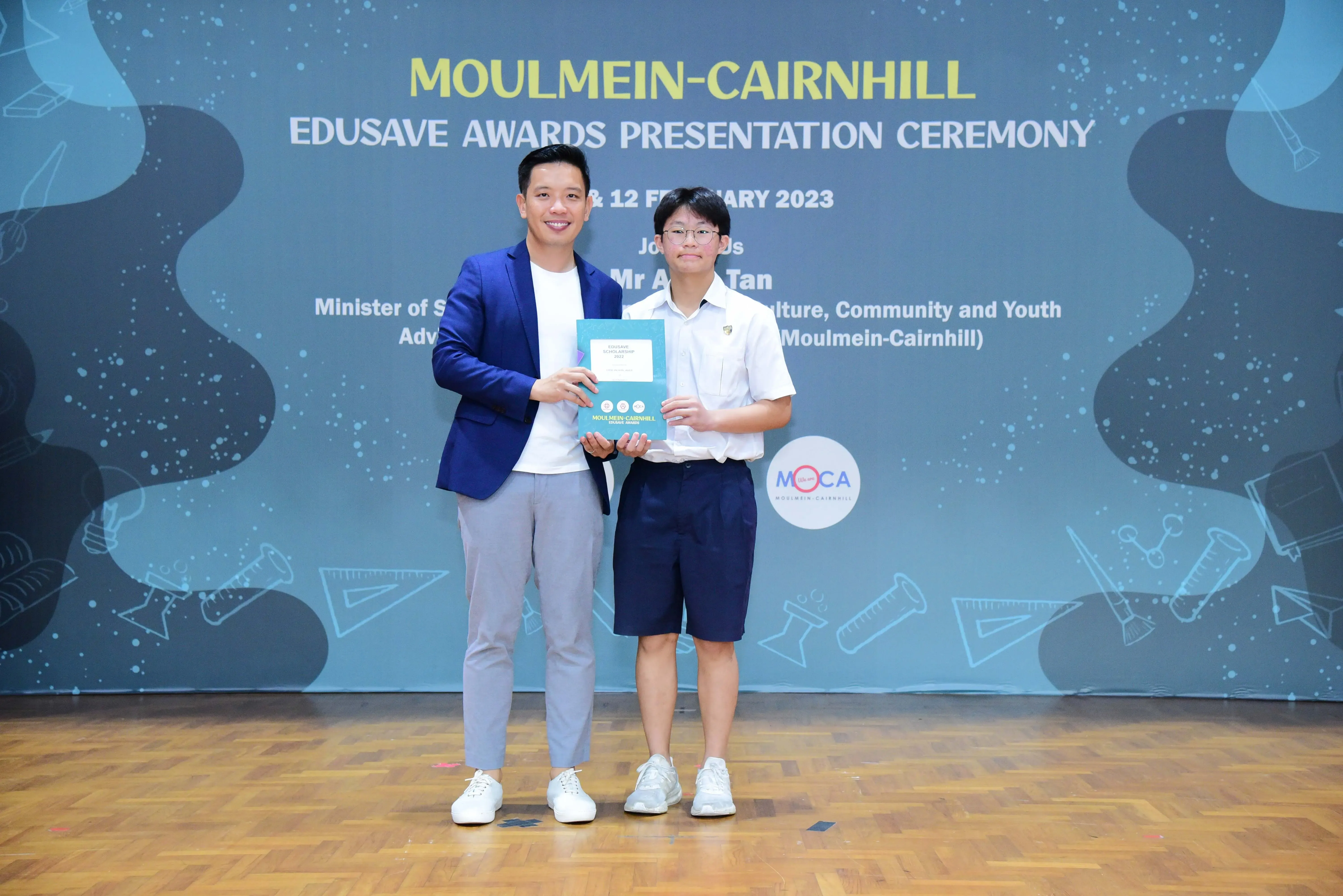 Two people holding an award booklet at the Moulmein-Cairnhill Edusave Awards Presentation Ceremony 2023.