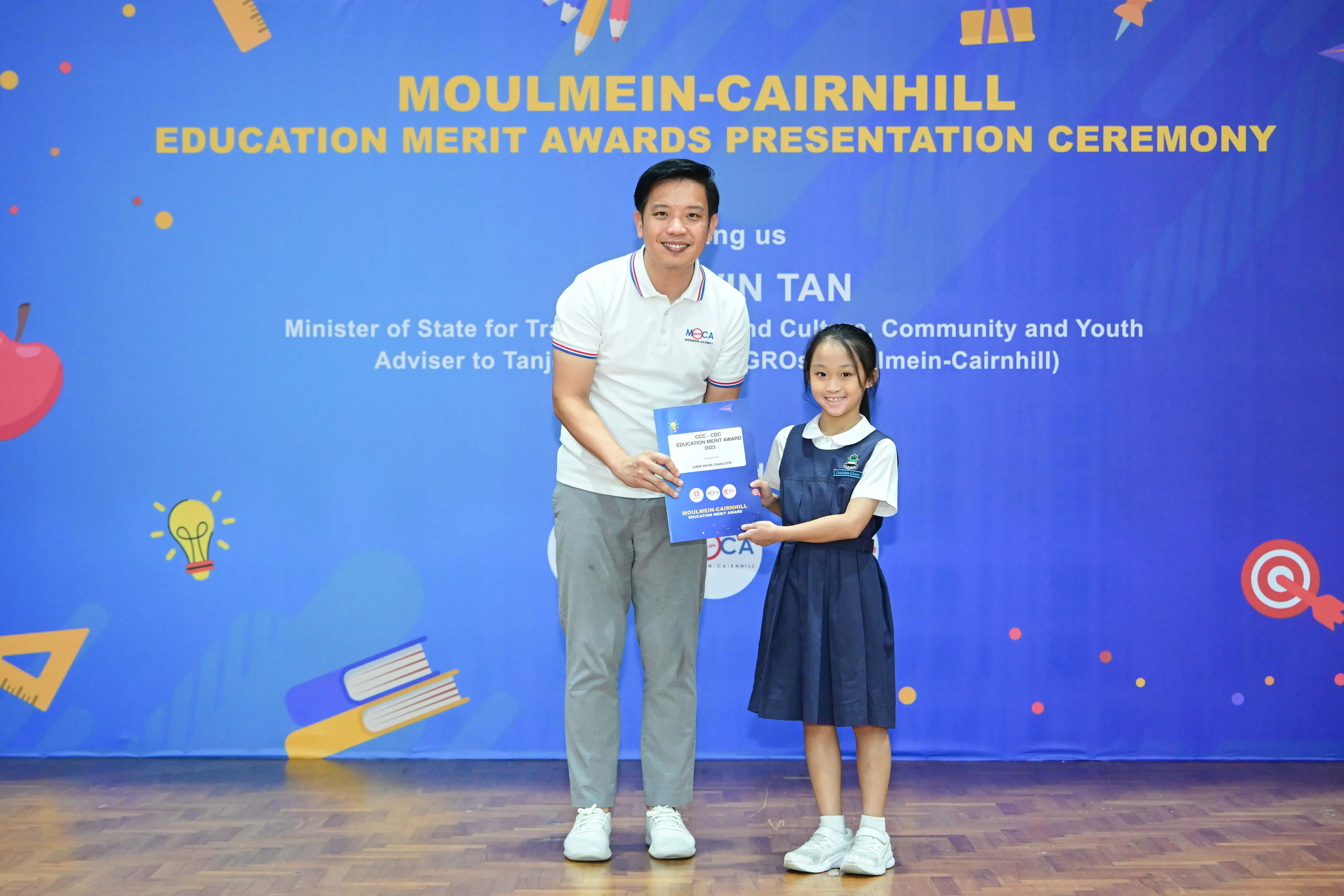 A man and a young girl in school uniform hold a certificate at the Moulmein-Cairnhill Education Merit Awards ceremony.