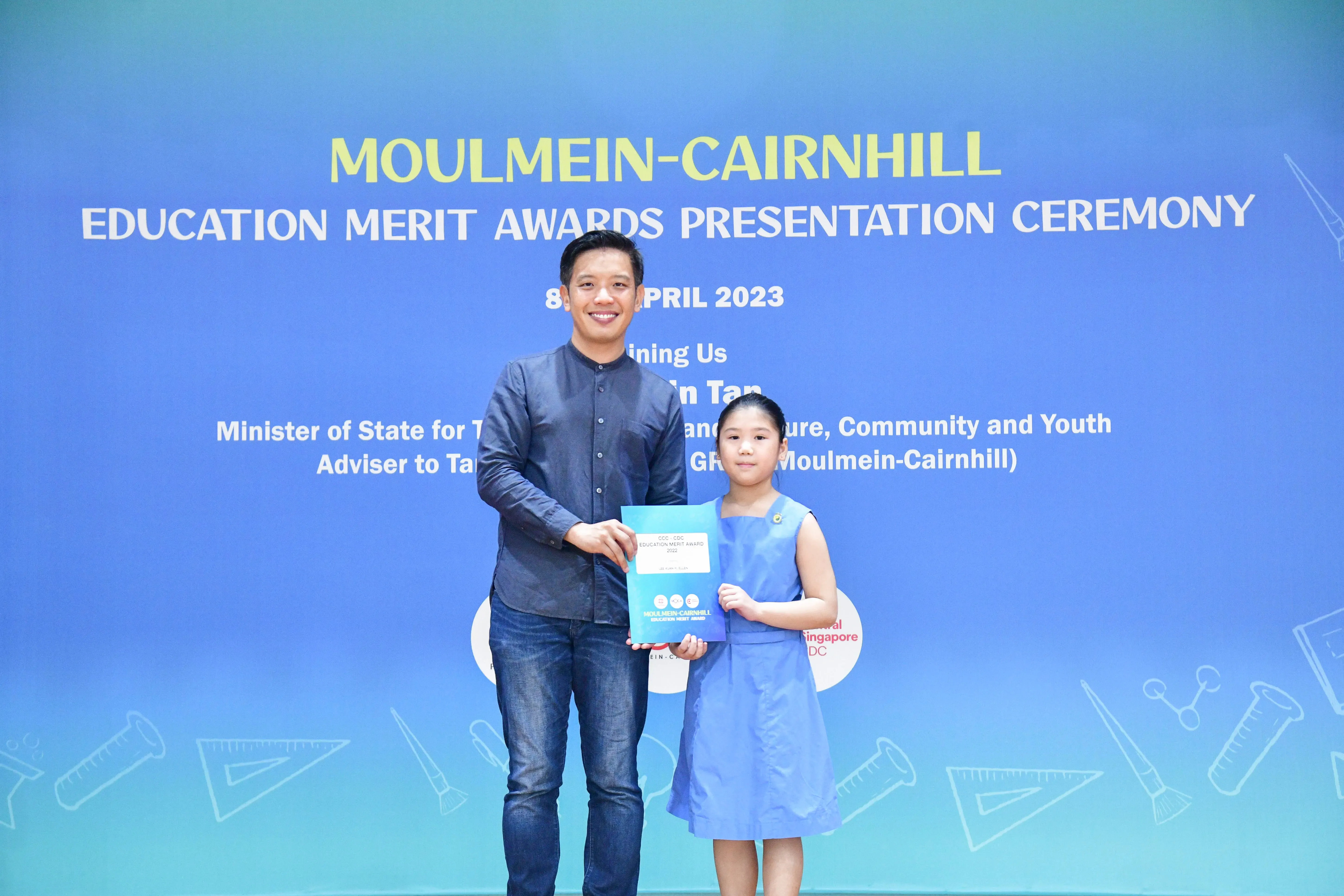 A man and a young girl hold a certificate together at the Moulmein-Cairnhill Education Merit Awards Ceremony, April 2023.