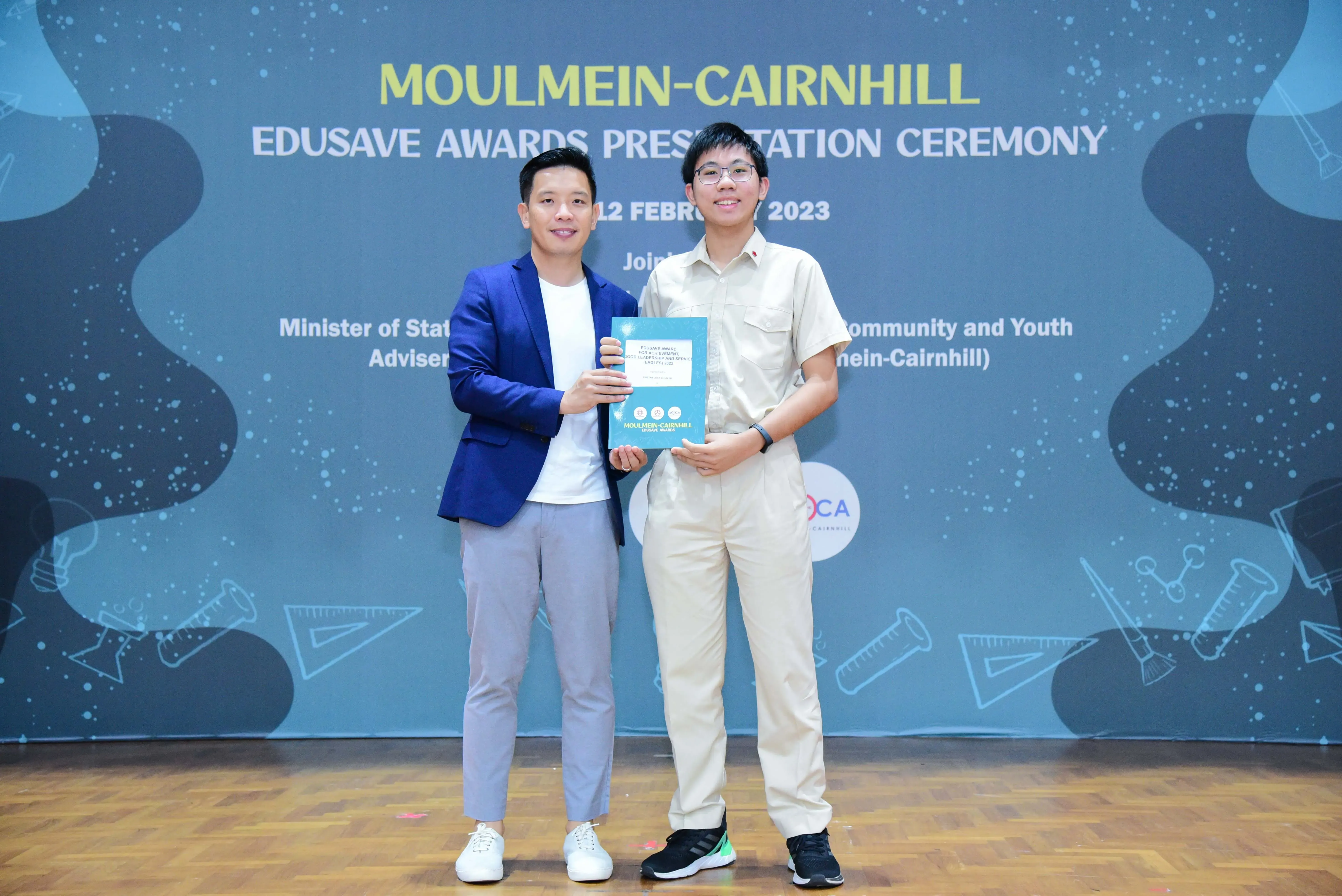Two men pose holding an award booklet at the Moulmein-Cairnhill Edusave Awards Presentation Ceremony 2023.