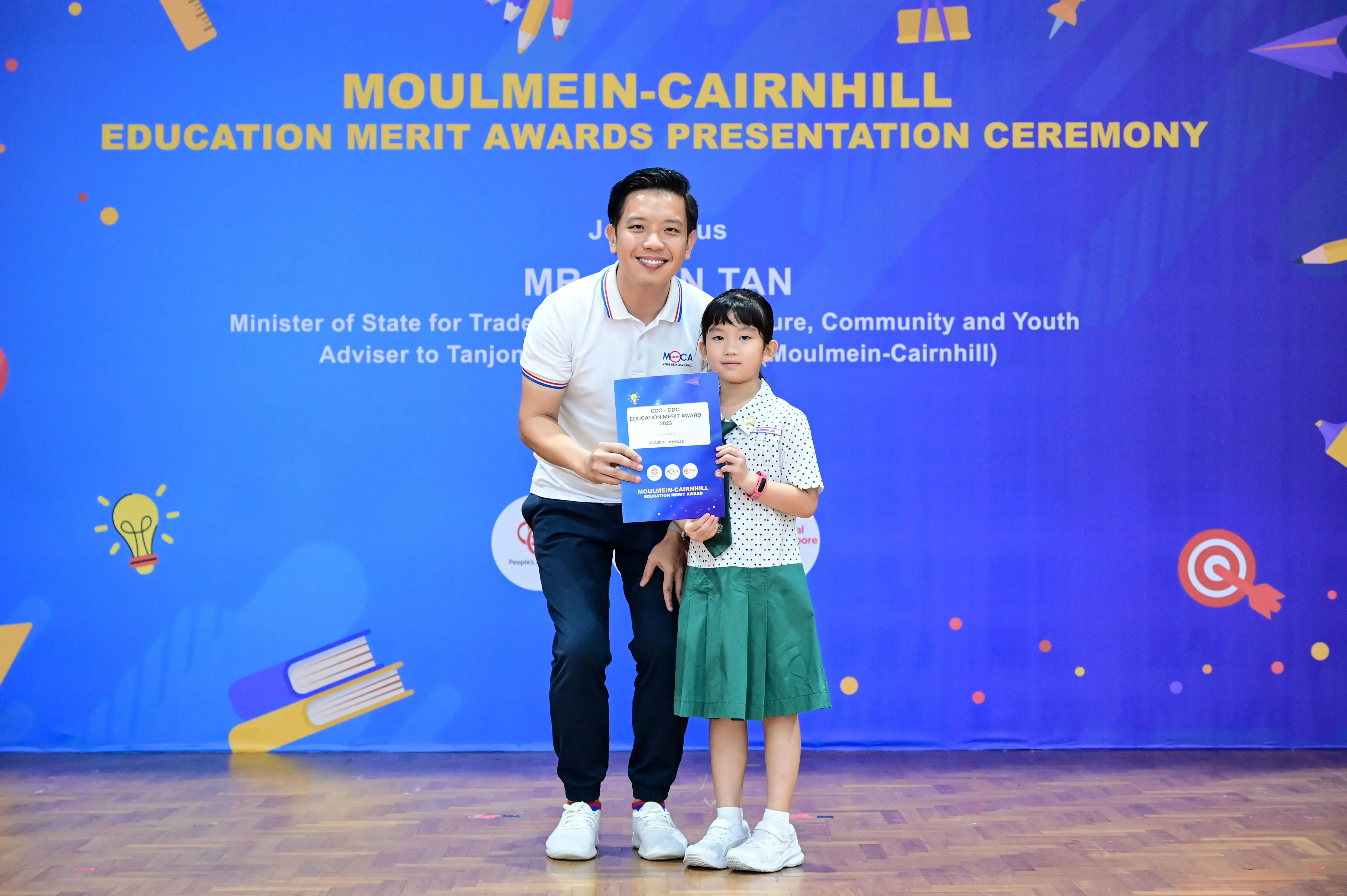A man and a young girl hold a certificate together at the Moulmein-Cairnhill Education Merit Awards ceremony.