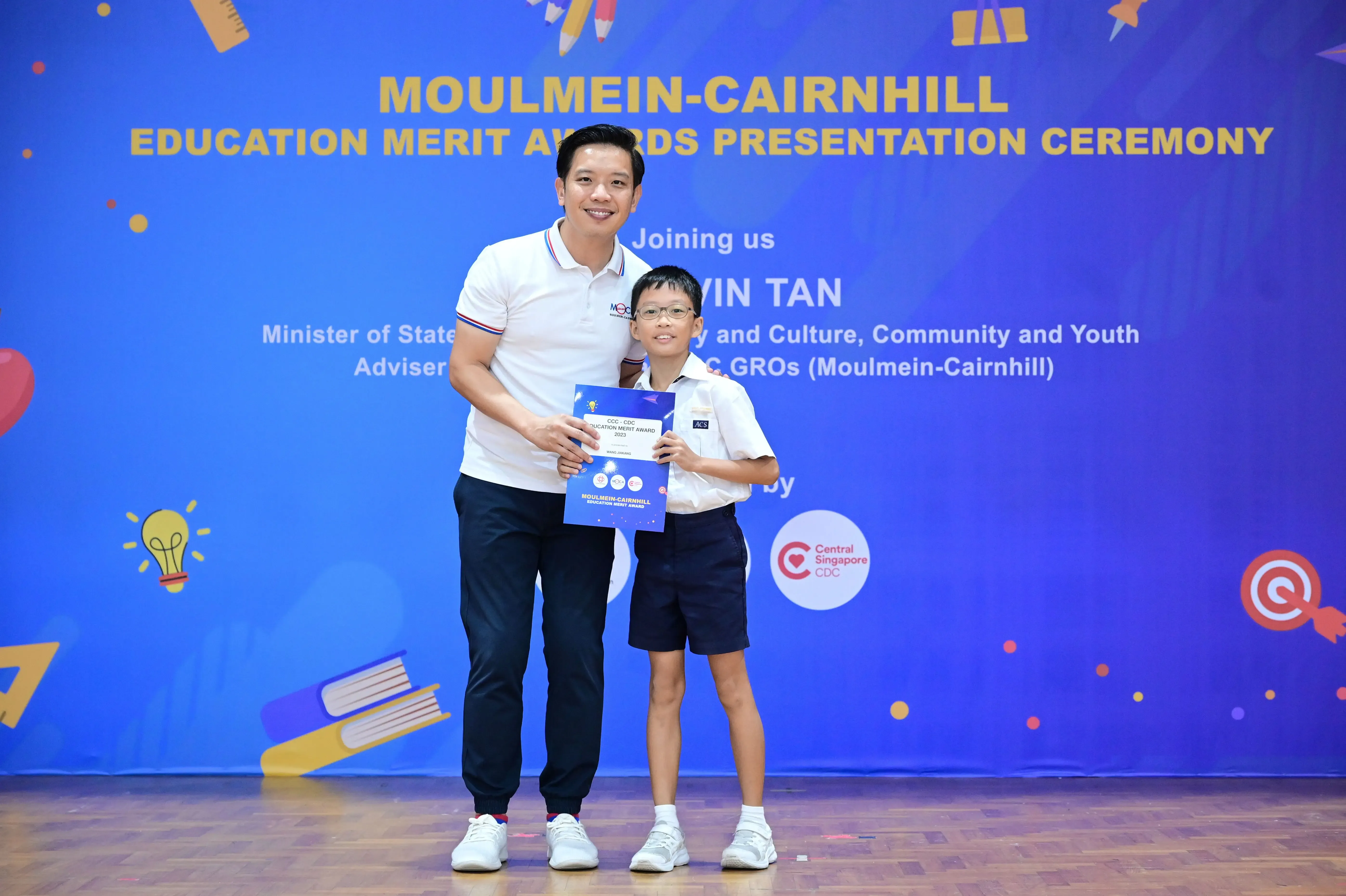 A man and a young boy holding a certificate at the Moulmein-Cairnhill Education Merit Awards Presentation Ceremony.