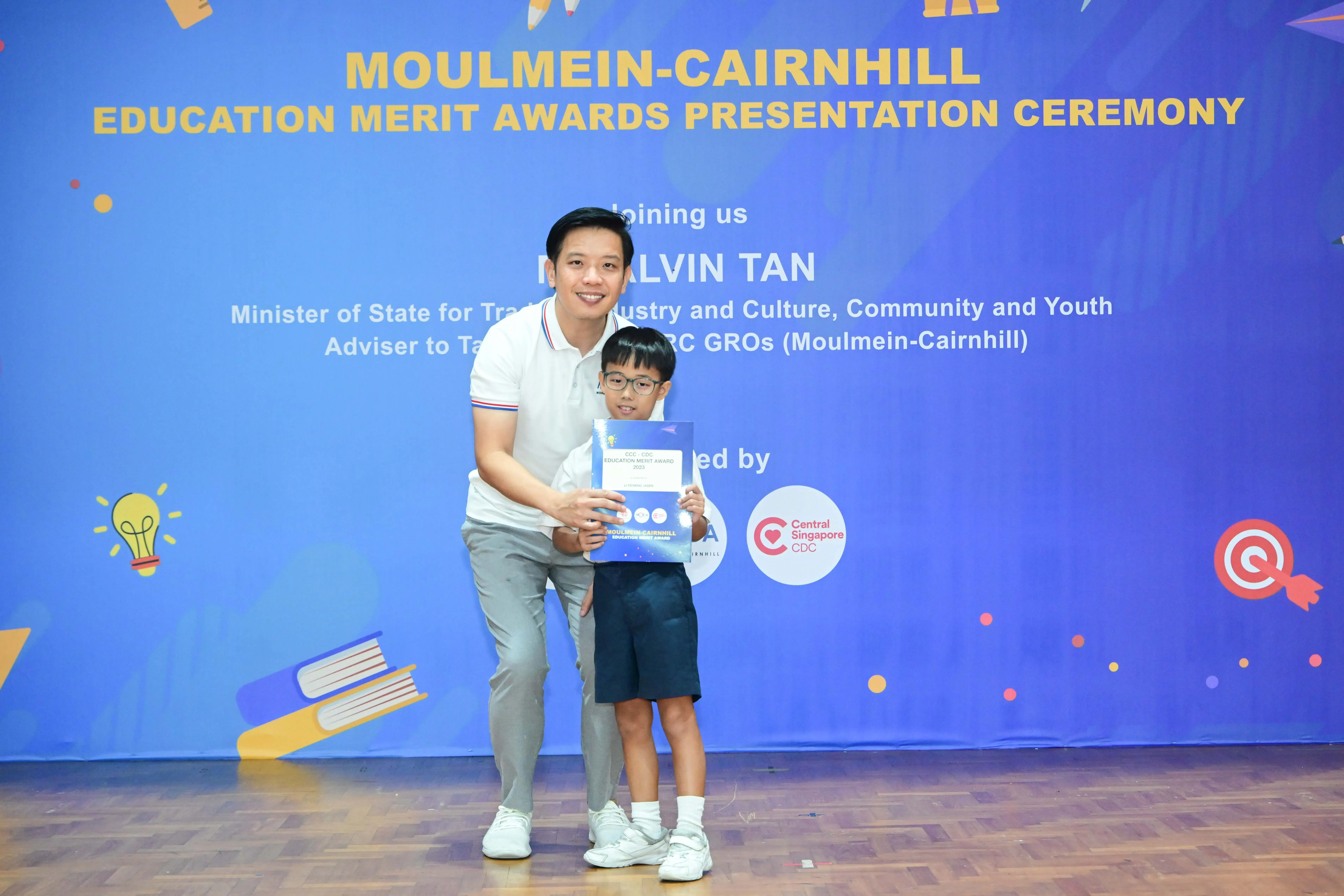 A man and a young boy hold an award certificate at the Moulmein-Cairnhill Education Merit Awards Presentation Ceremony.