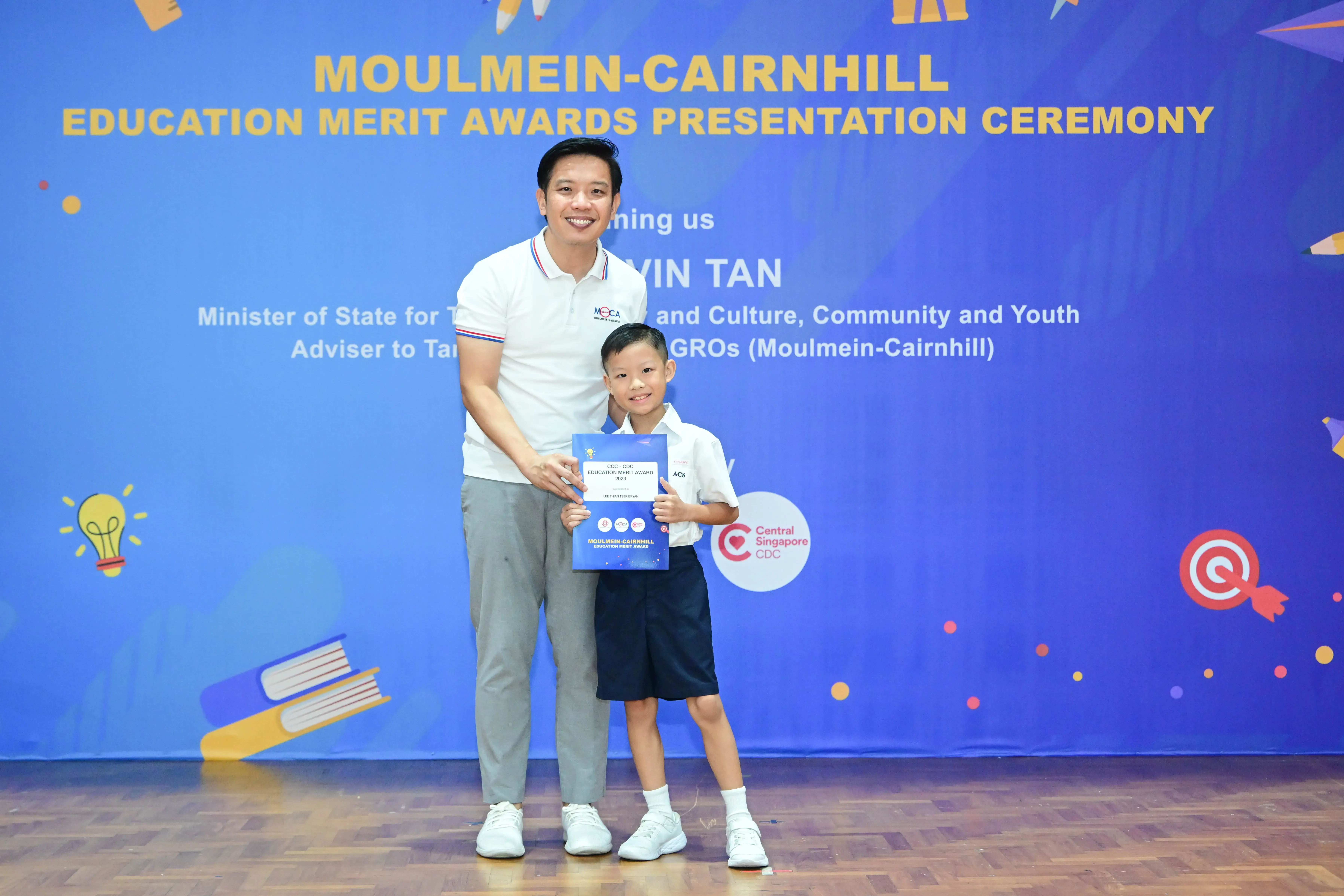 A man and young boy hold an award certificate at the Moulmein-Cairnhill Education Merit Awards Presentation Ceremony.