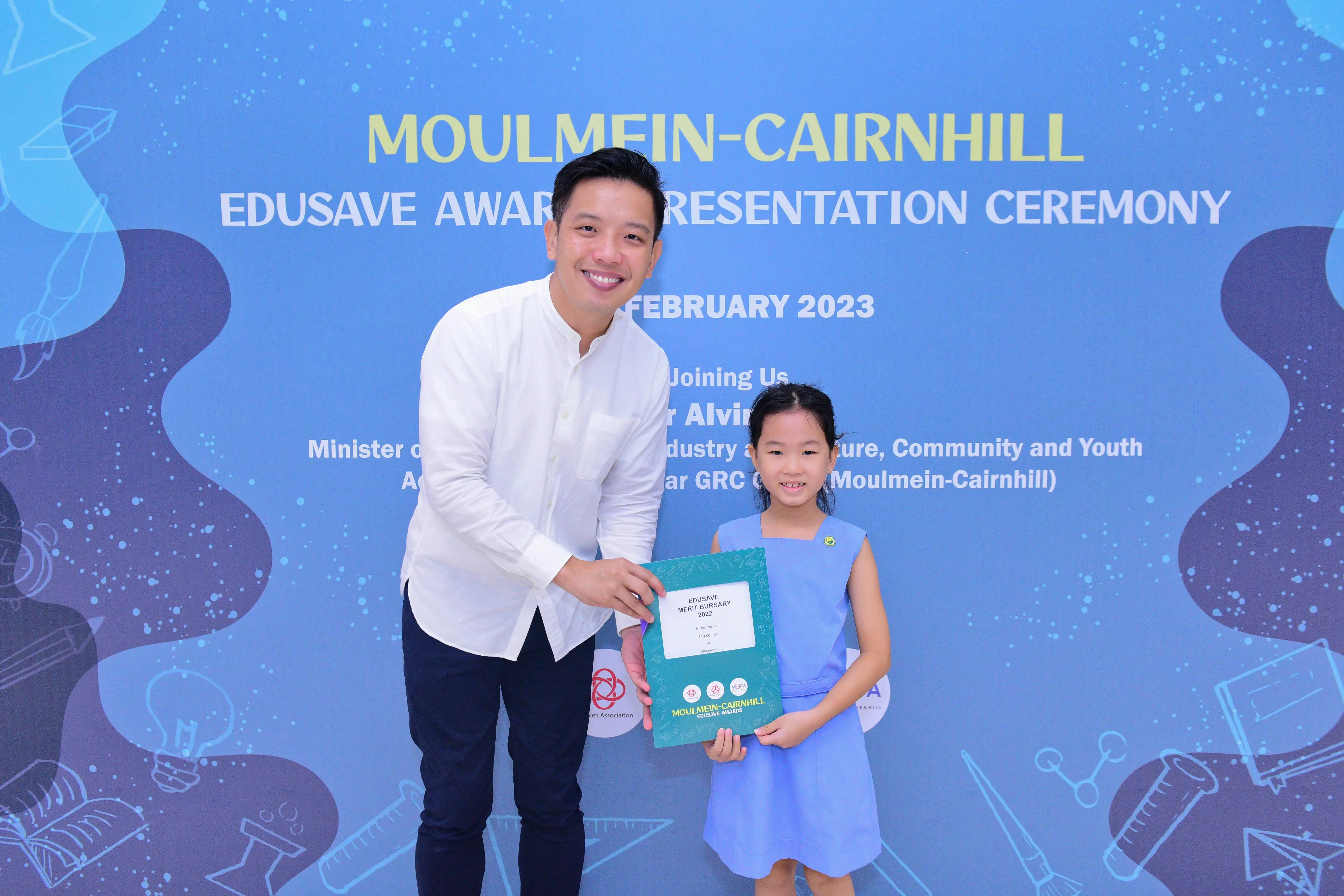 A man and a young girl hold an Edusave Merit Bursary certificate at the Moulmein-Cairnhill Awards Ceremony, February 2023.