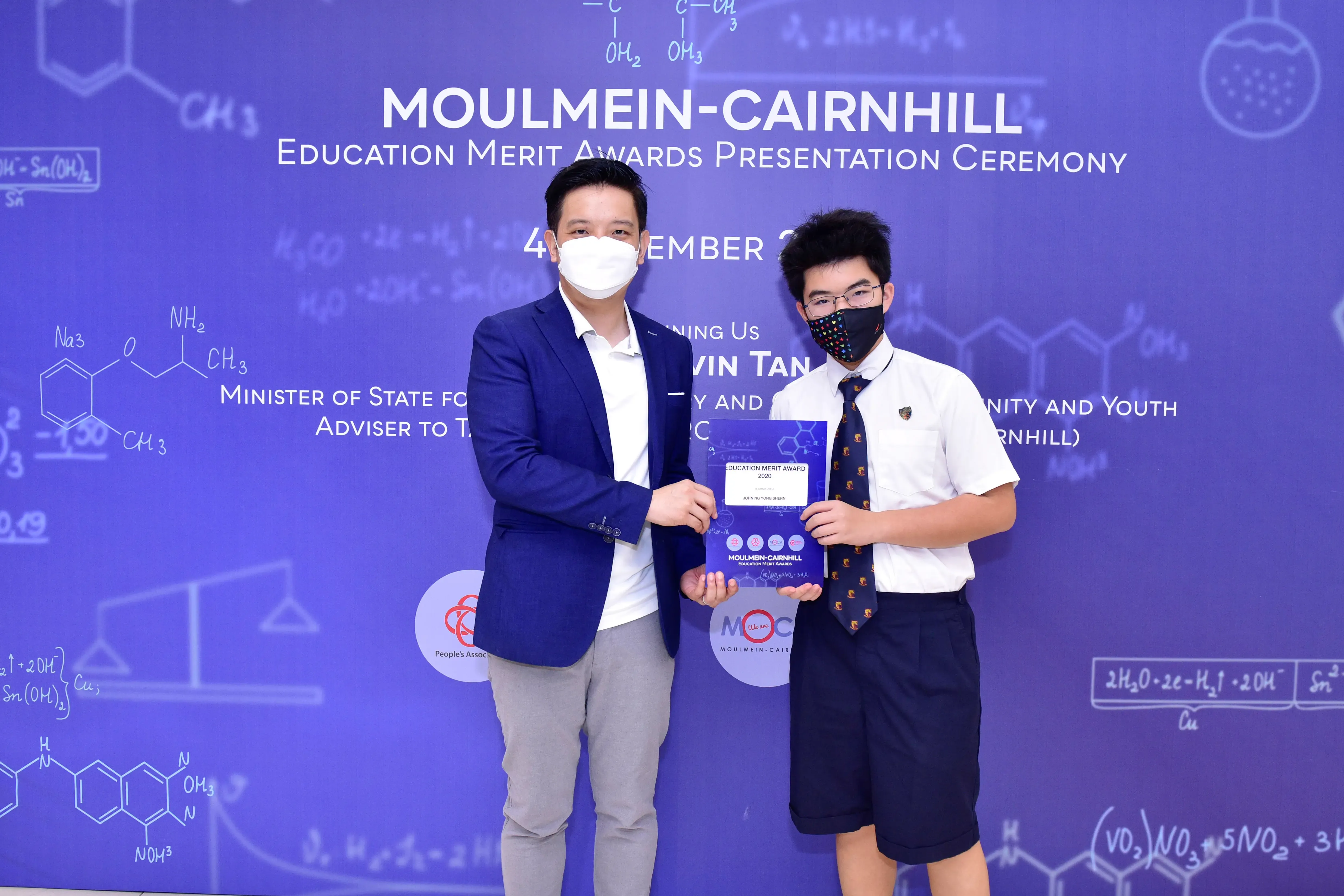 Two masked individuals hold an award certificate at the Moulmein-Cairnhill Education Merit Awards Presentation Ceremony.