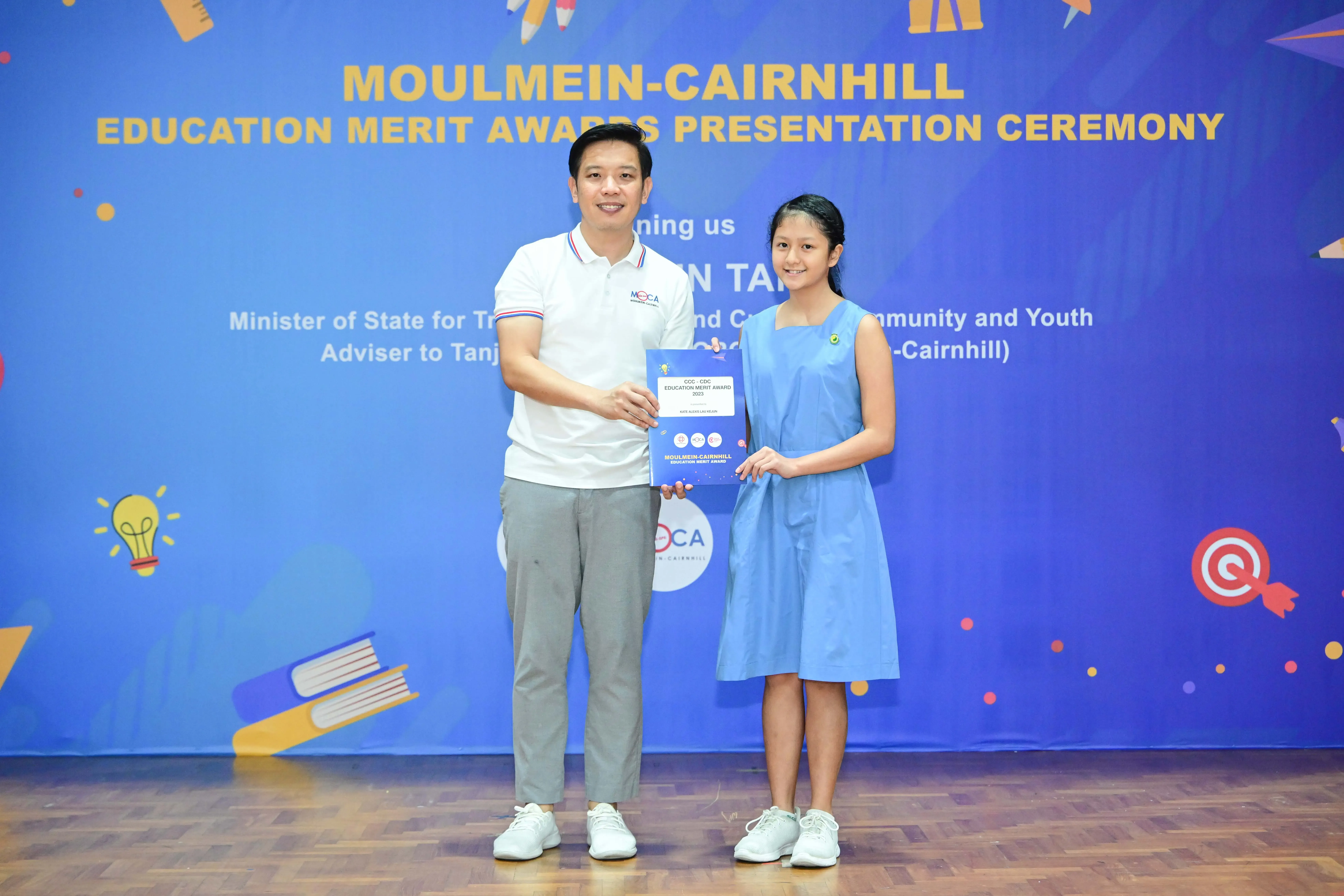 Man and young girl hold an award certificate at the Moulmein-Cairnhill Education Merit Awards Presentation Ceremony.