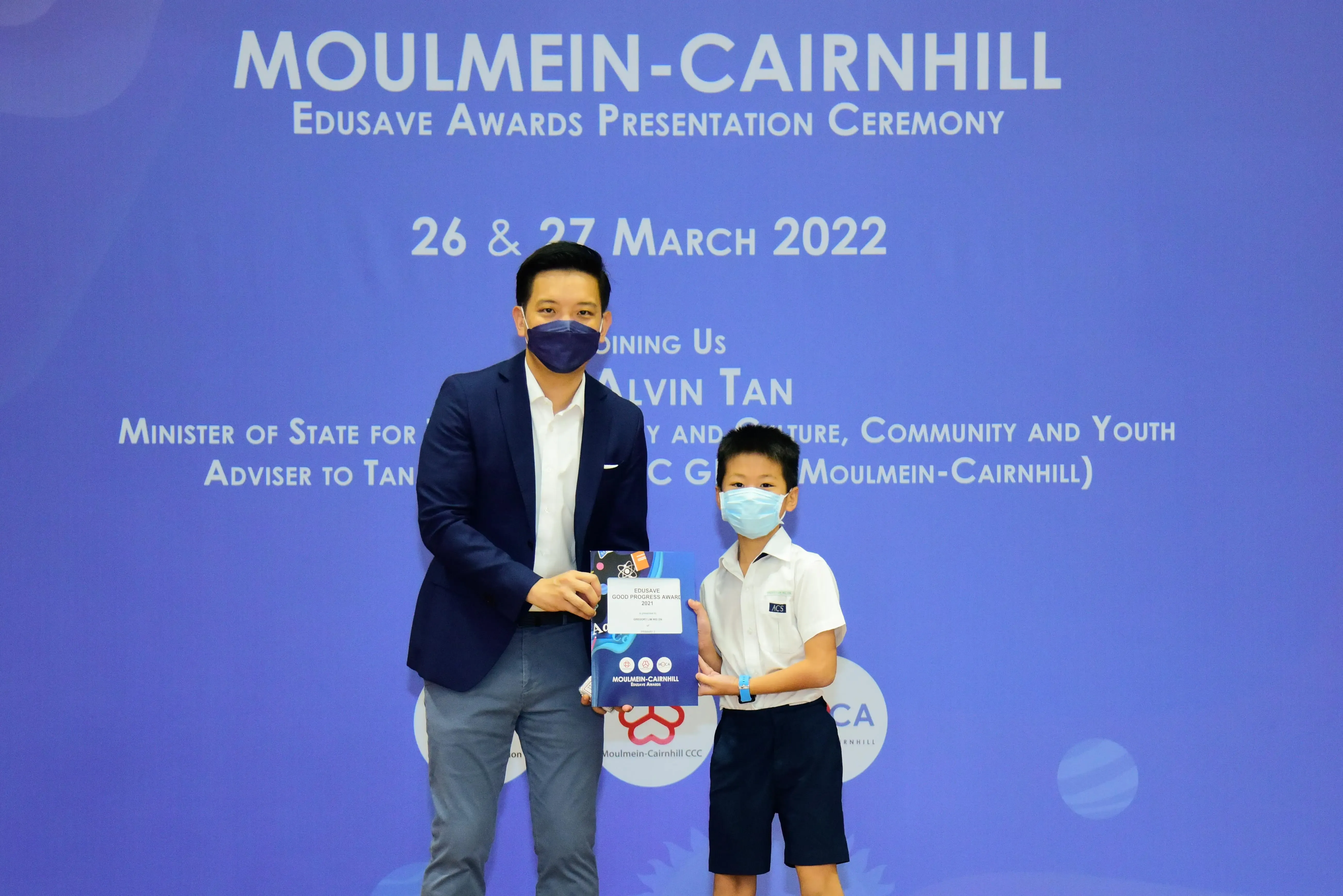 An adult and a young boy in masks hold an award at the Moulmein-Cairnhill Edusave Awards Ceremony, March 2022.