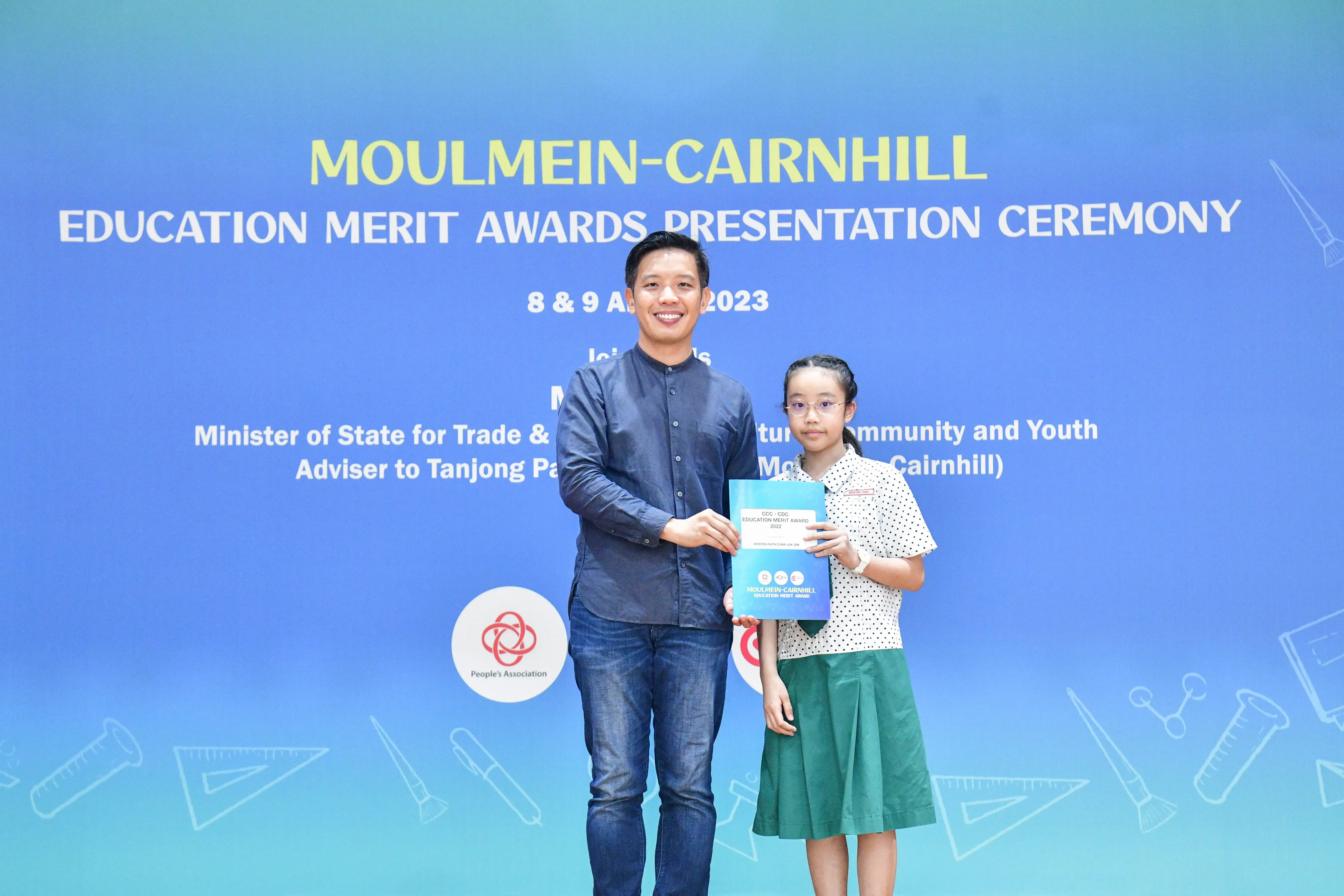 A man and a young girl hold an award certificate at the Moulmein-Cairnhill Education Merit Awards Ceremony 2023.