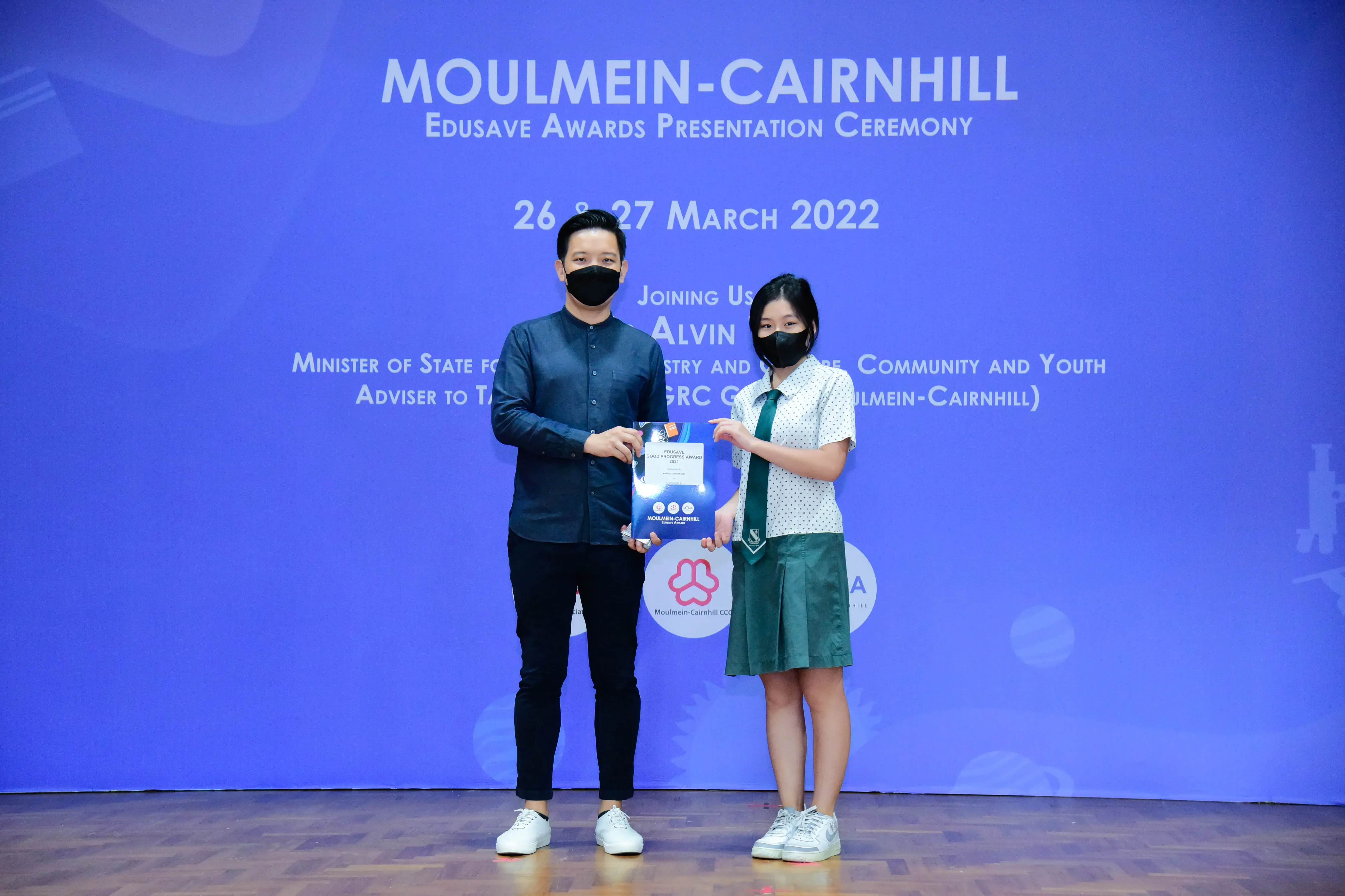 Two masked people hold an award booklet at the Moulmein-Cairnhill Edusave Awards Ceremony on March 26-27, 2022.