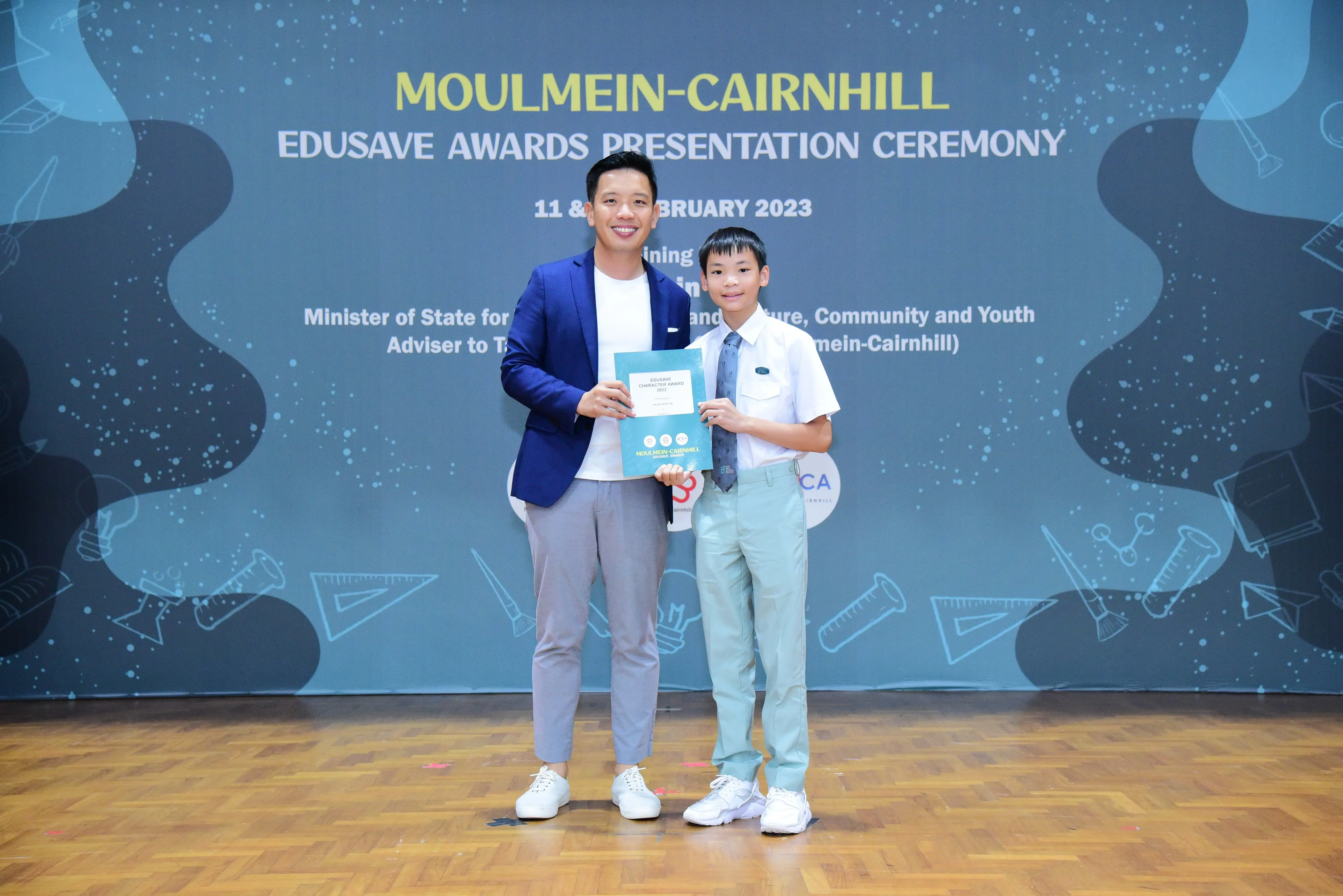 Man in blue blazer and young boy in school uniform hold a certificate at Moulmein-Cairnhill Edusave Awards 2023.