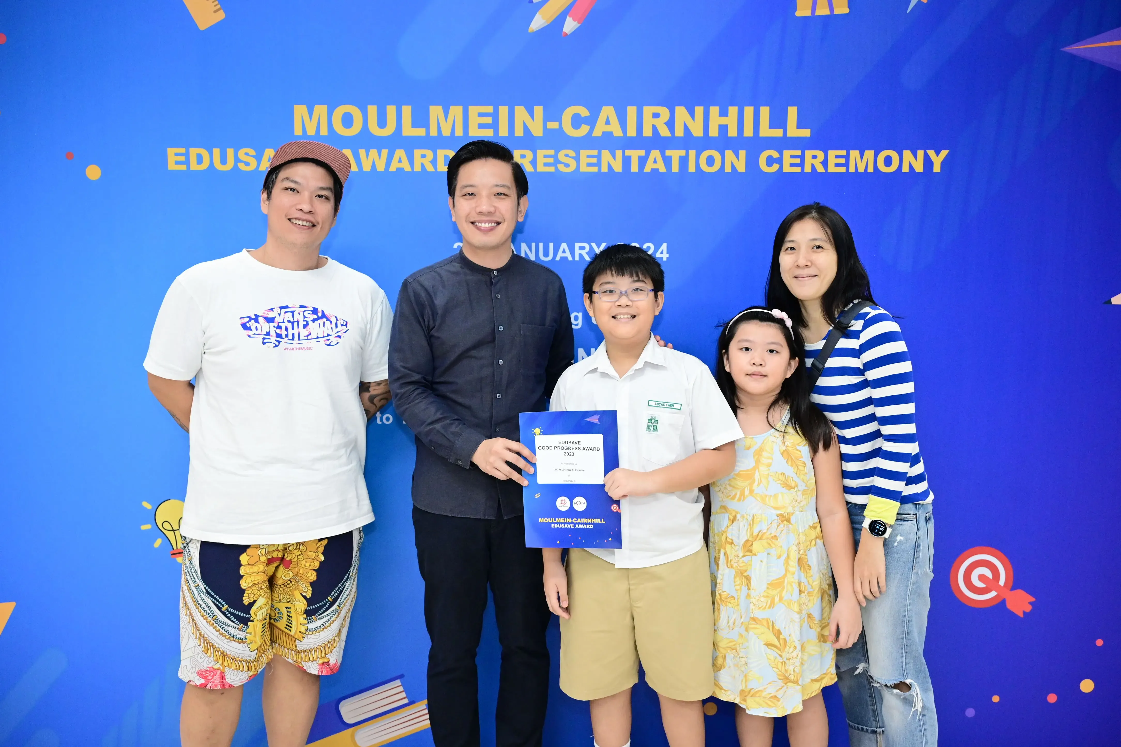 Five people pose at the Moulmein-Cairnhill Edusave Award Presentation Ceremony, with a boy holding a certificate.