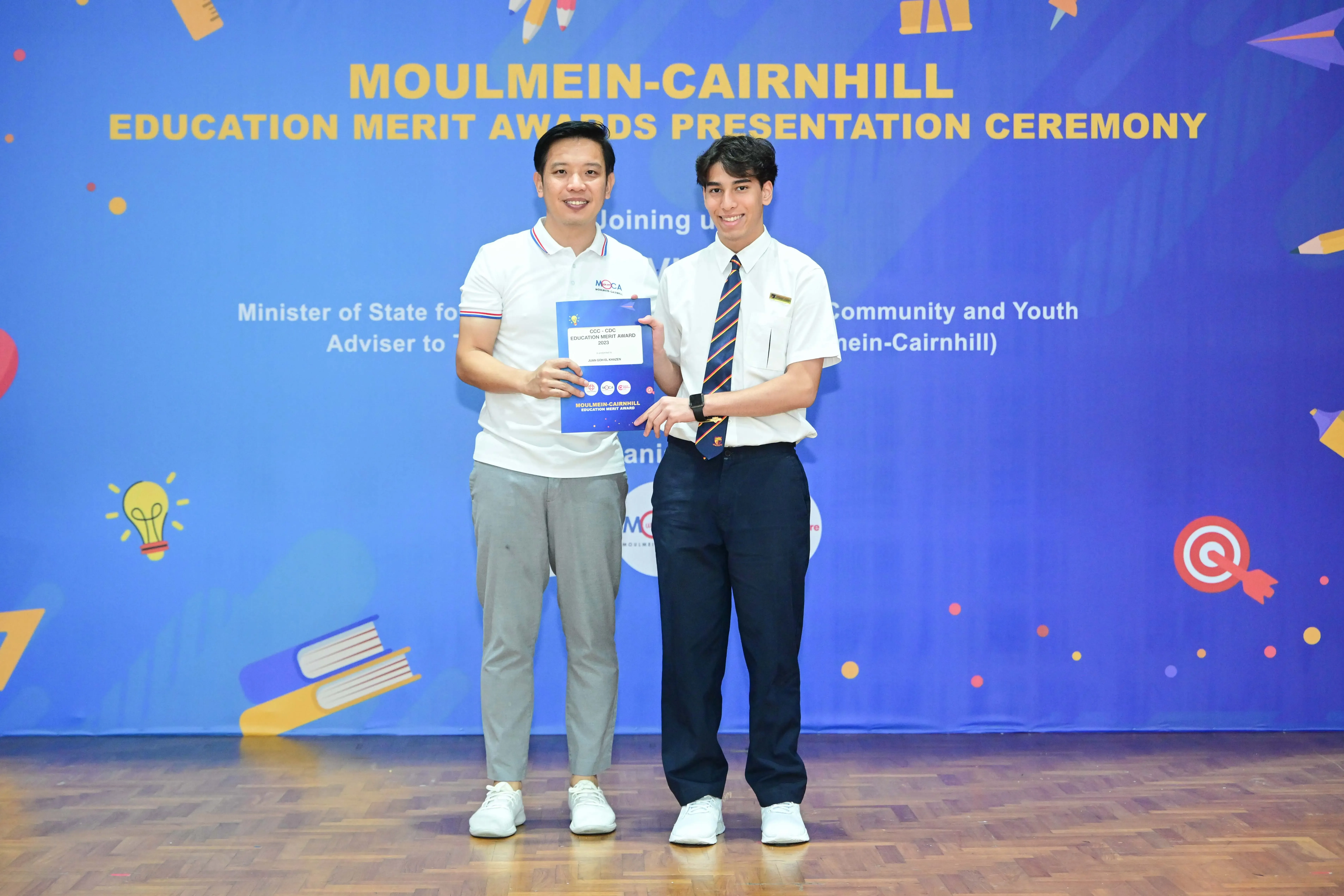 Two men hold a certificate together at the Moulmein-Cairnhill Education Merit Awards Presentation Ceremony.