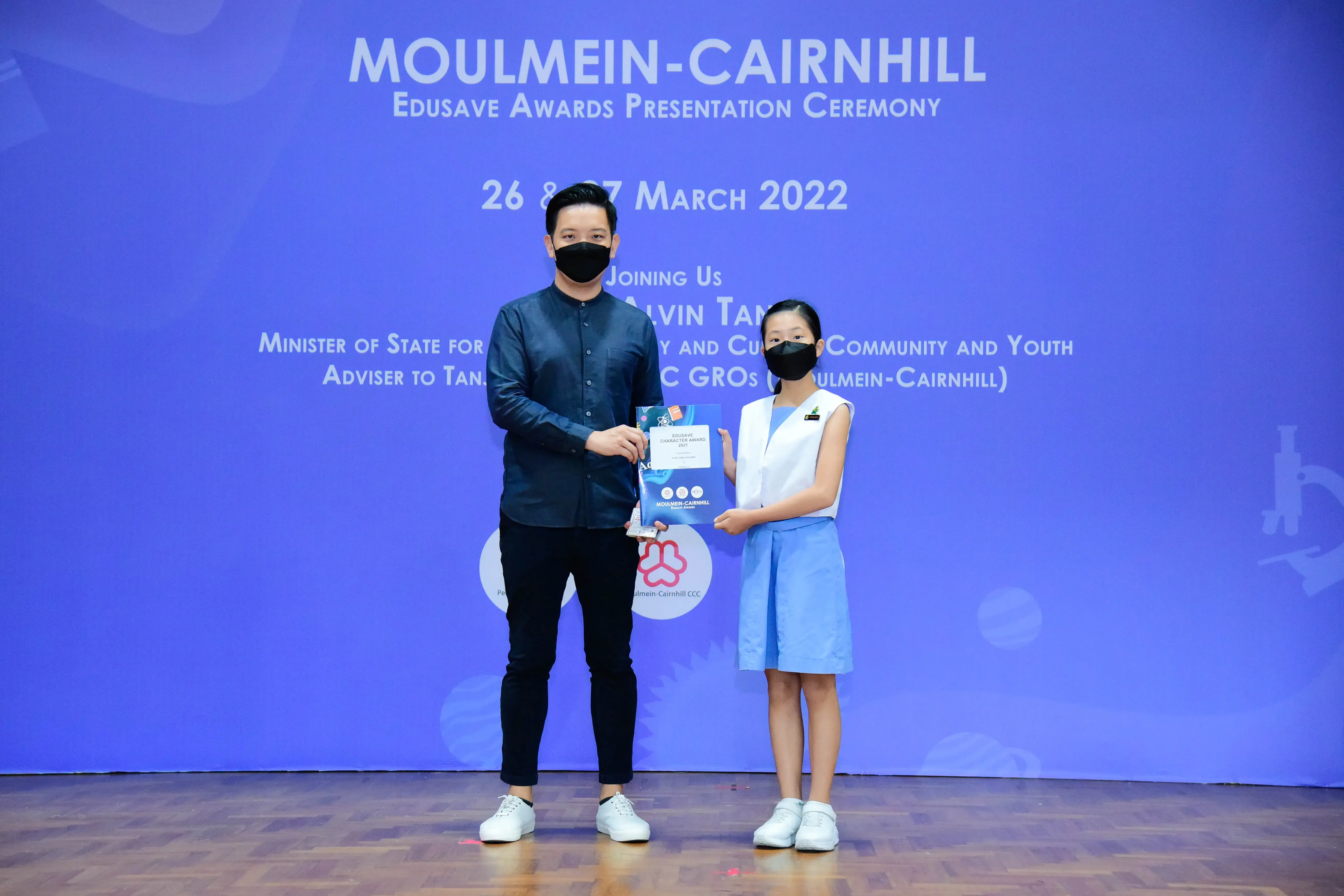 Man and young girl in masks hold an award at Moulmein-Cairnhill Edusave Awards Ceremony, March 2022.