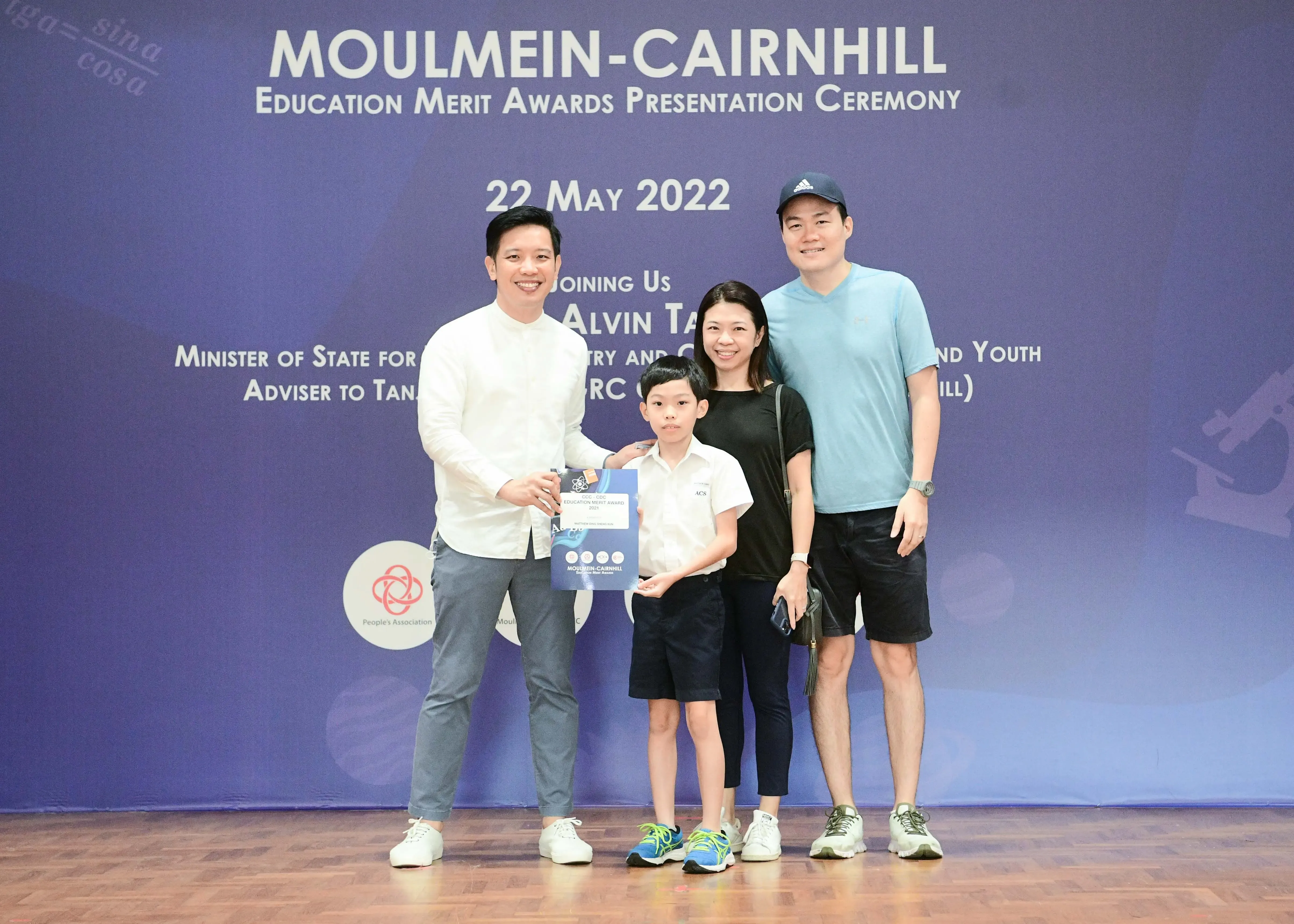 Four people pose at the Moulmein-Cairnhill Education Merit Awards Ceremony on 22 May 2022, with a boy holding a certificate.