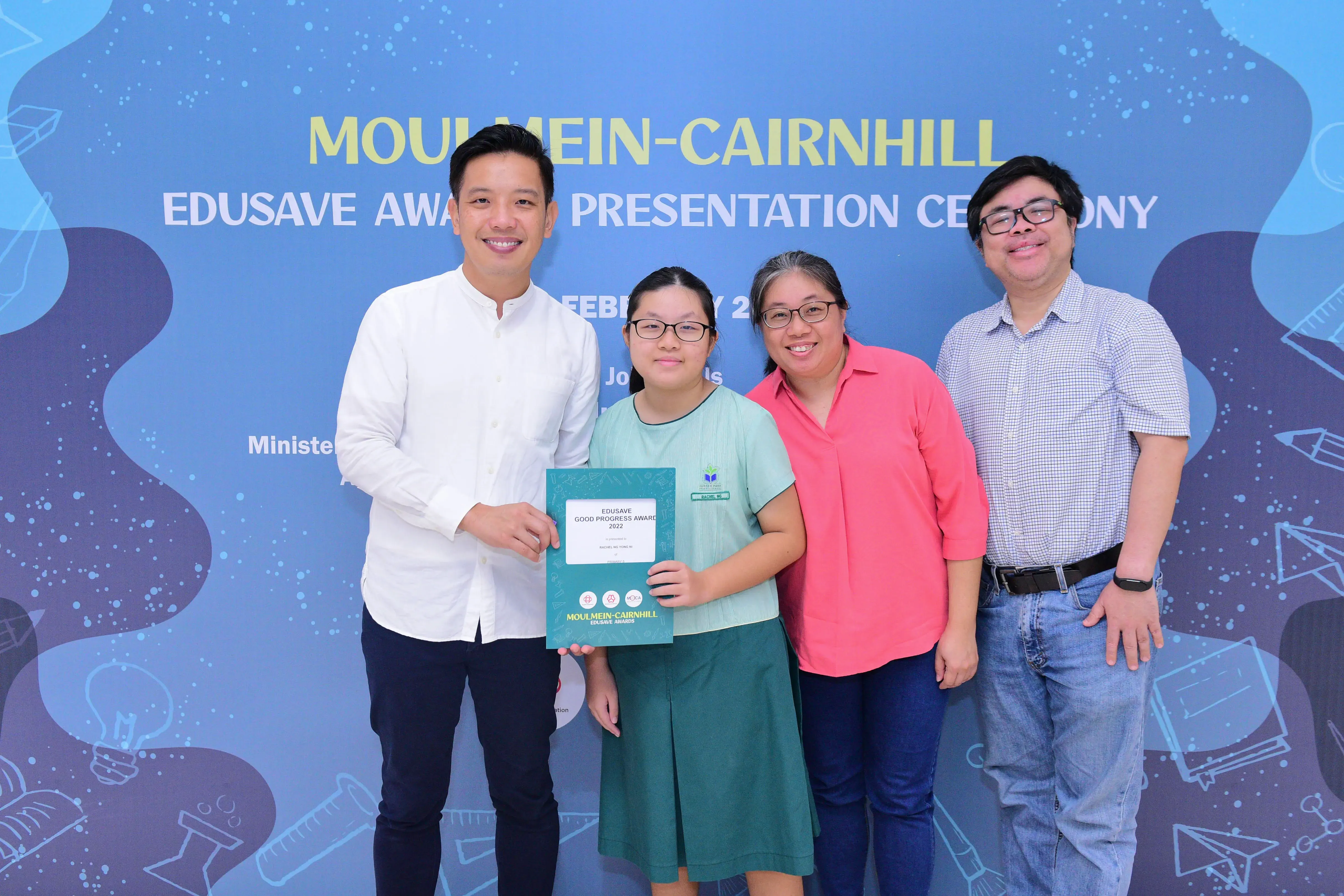 Four people pose at the Moulmein-Cairnhill Edusave Award Presentation Ceremony, with a student holding an award certificate.
