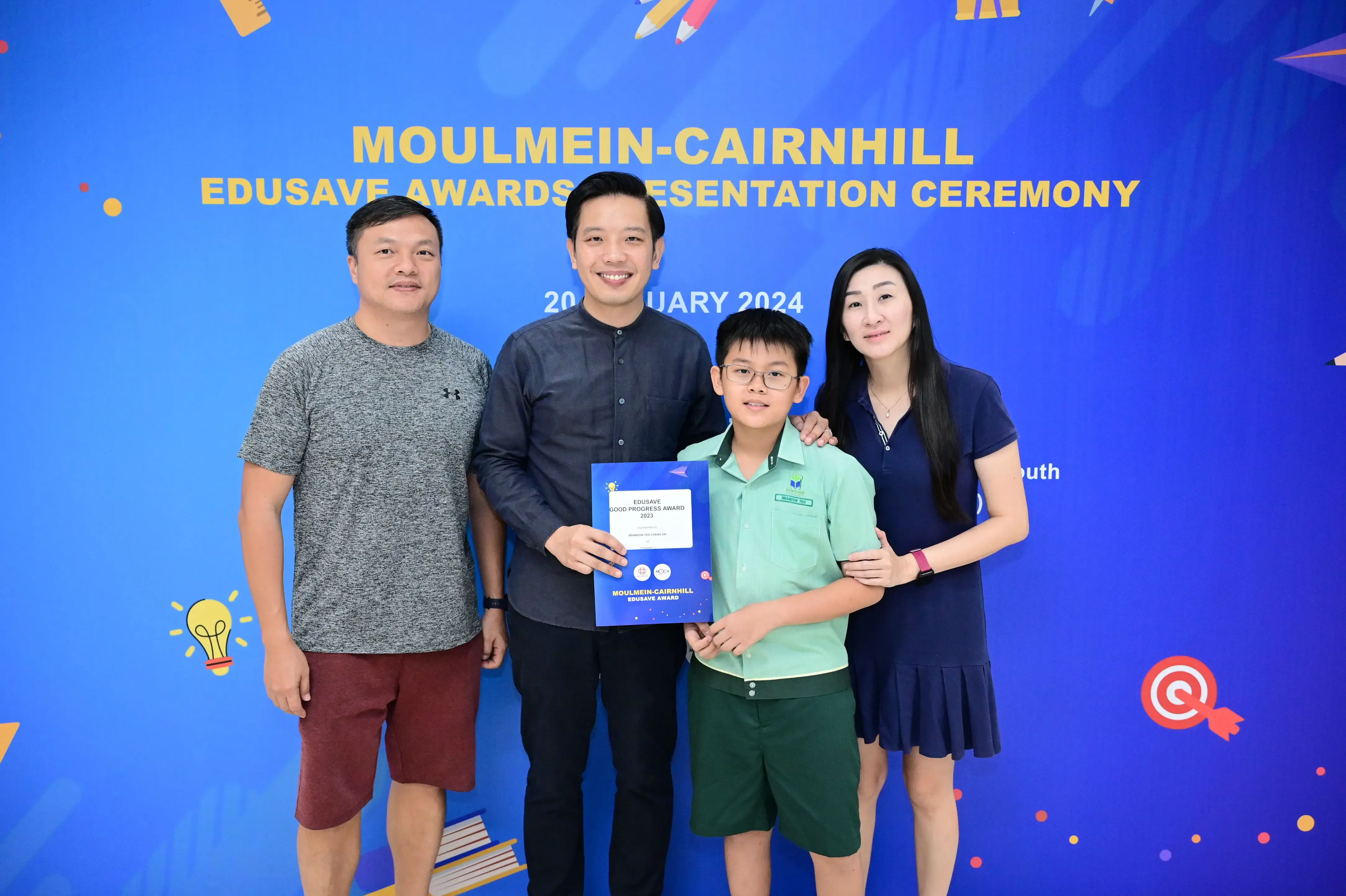 Three adults and a boy holding an Edusave award certificate pose at the Moulmein-Cairnhill Awards Ceremony 2024.
