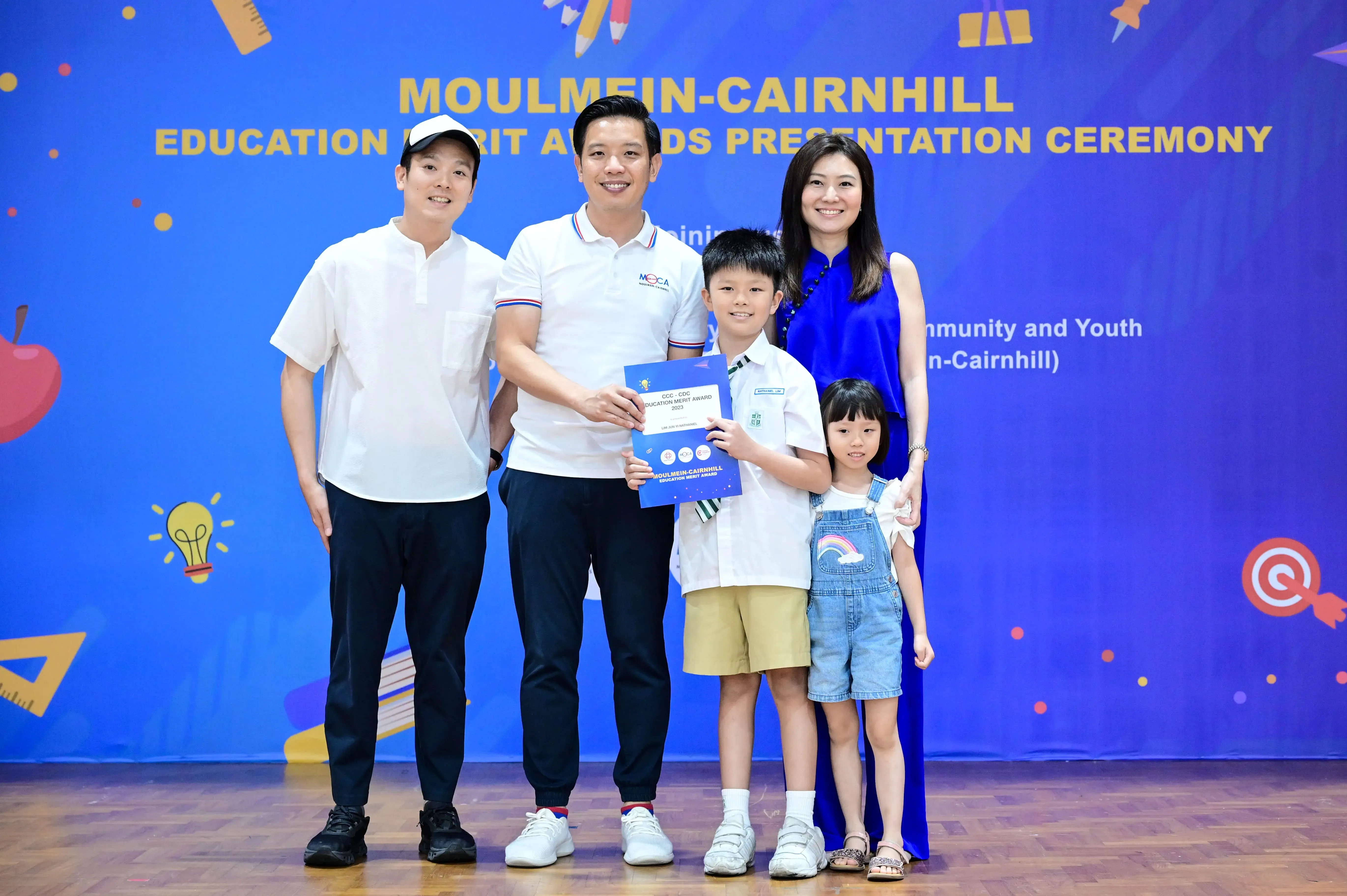 Five people pose at the Moulmein-Cairnhill Education Merit Awards ceremony, a boy holding an award certificate.