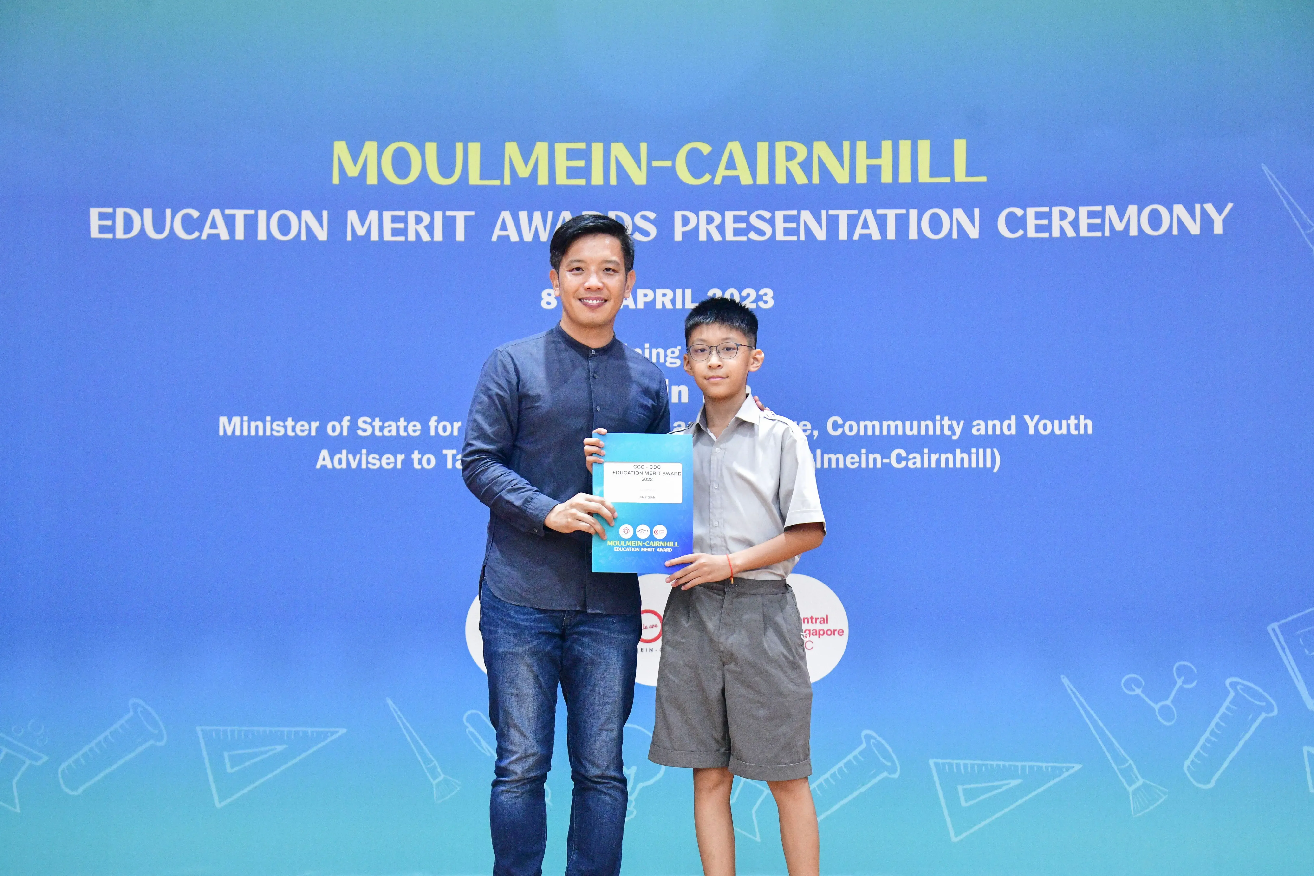 A man and a young boy hold a certificate together at the Moulmein-Cairnhill Education Merit Awards Ceremony, April 2023.