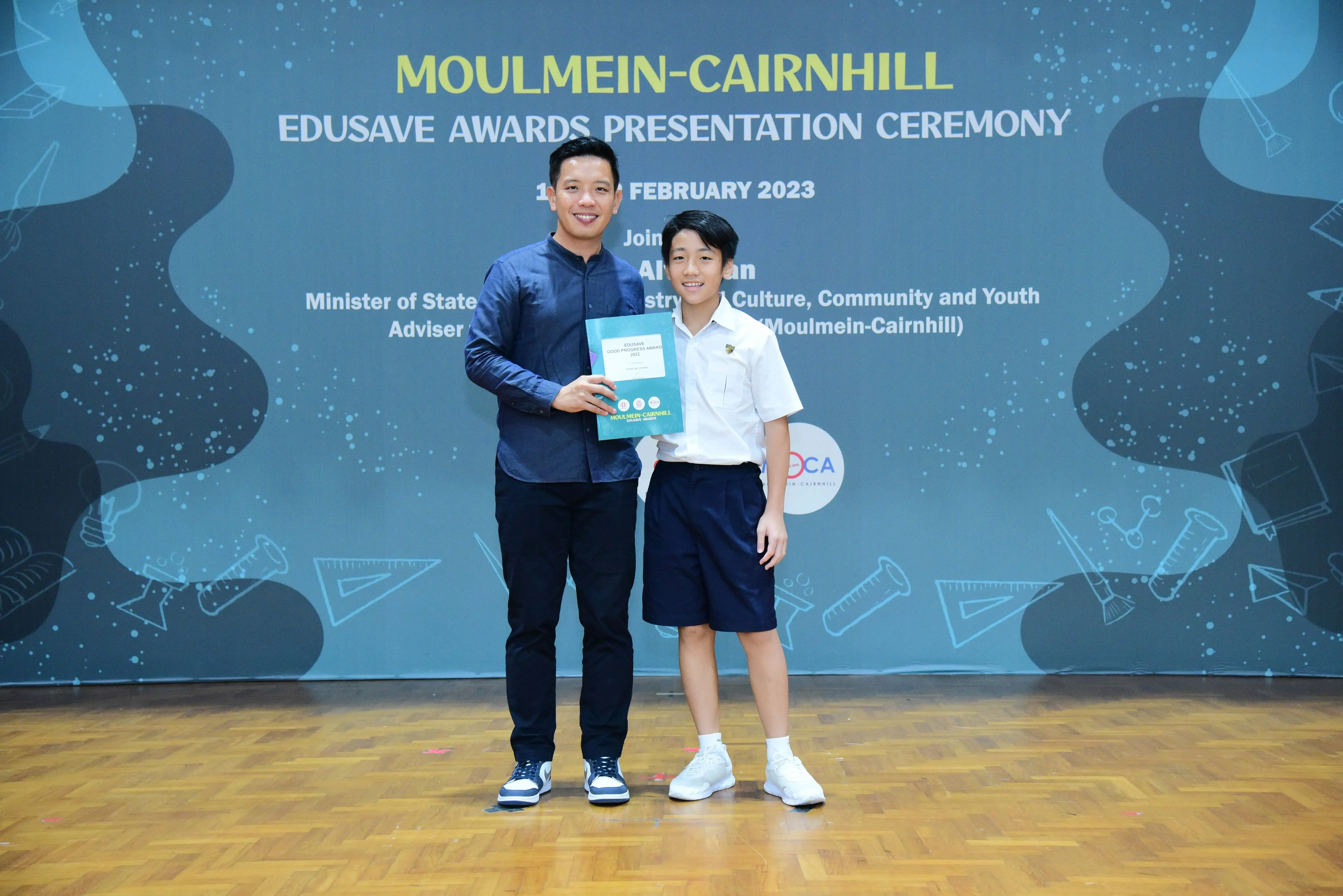 An adult and a uniformed student hold a certificate at the Moulmein-Cairnhill Edusave Awards Ceremony, February 2023.