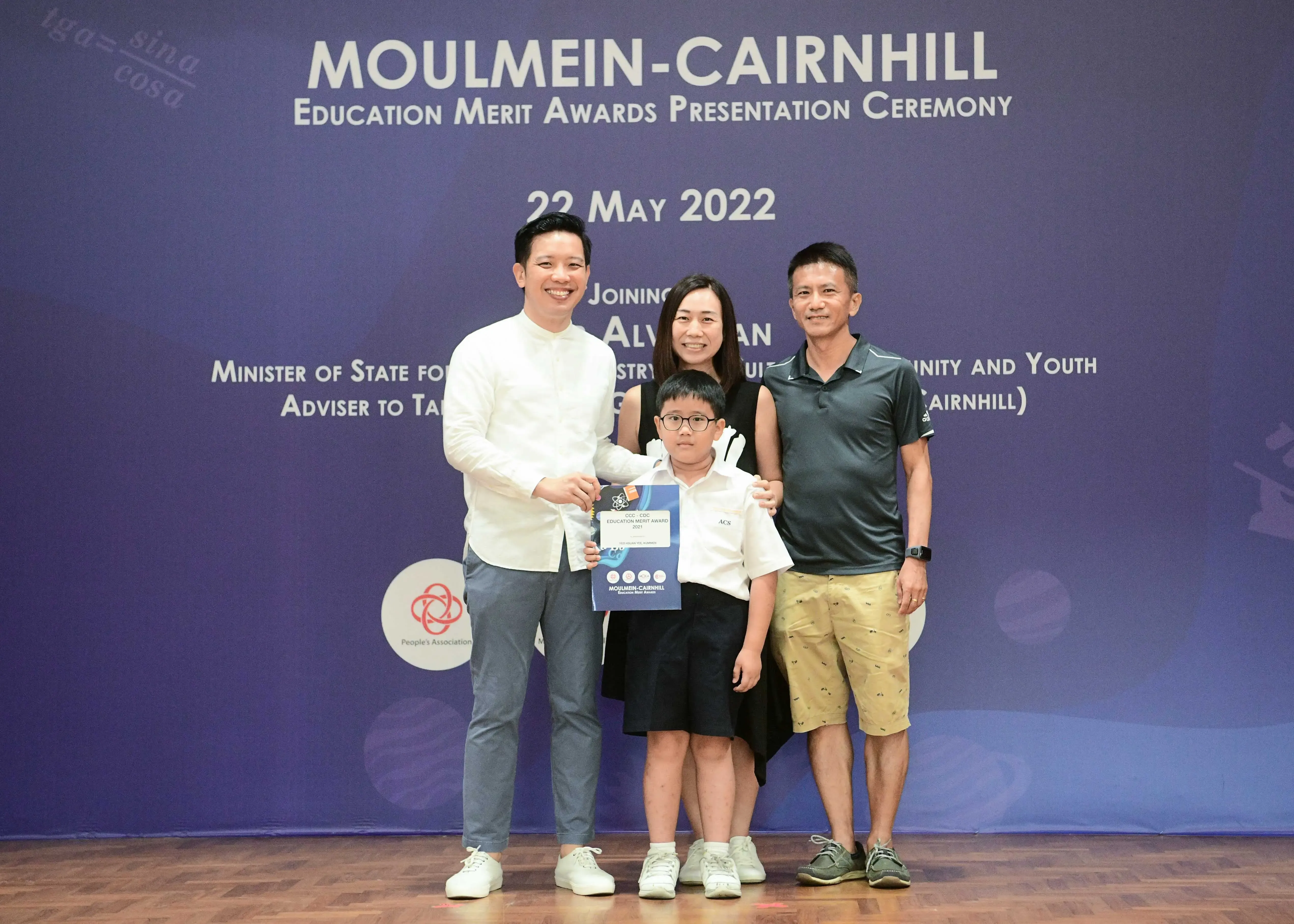 Four people pose at the Moulmein-Cairnhill Education Merit Awards ceremony on 22 May 2022, child holding a certificate.