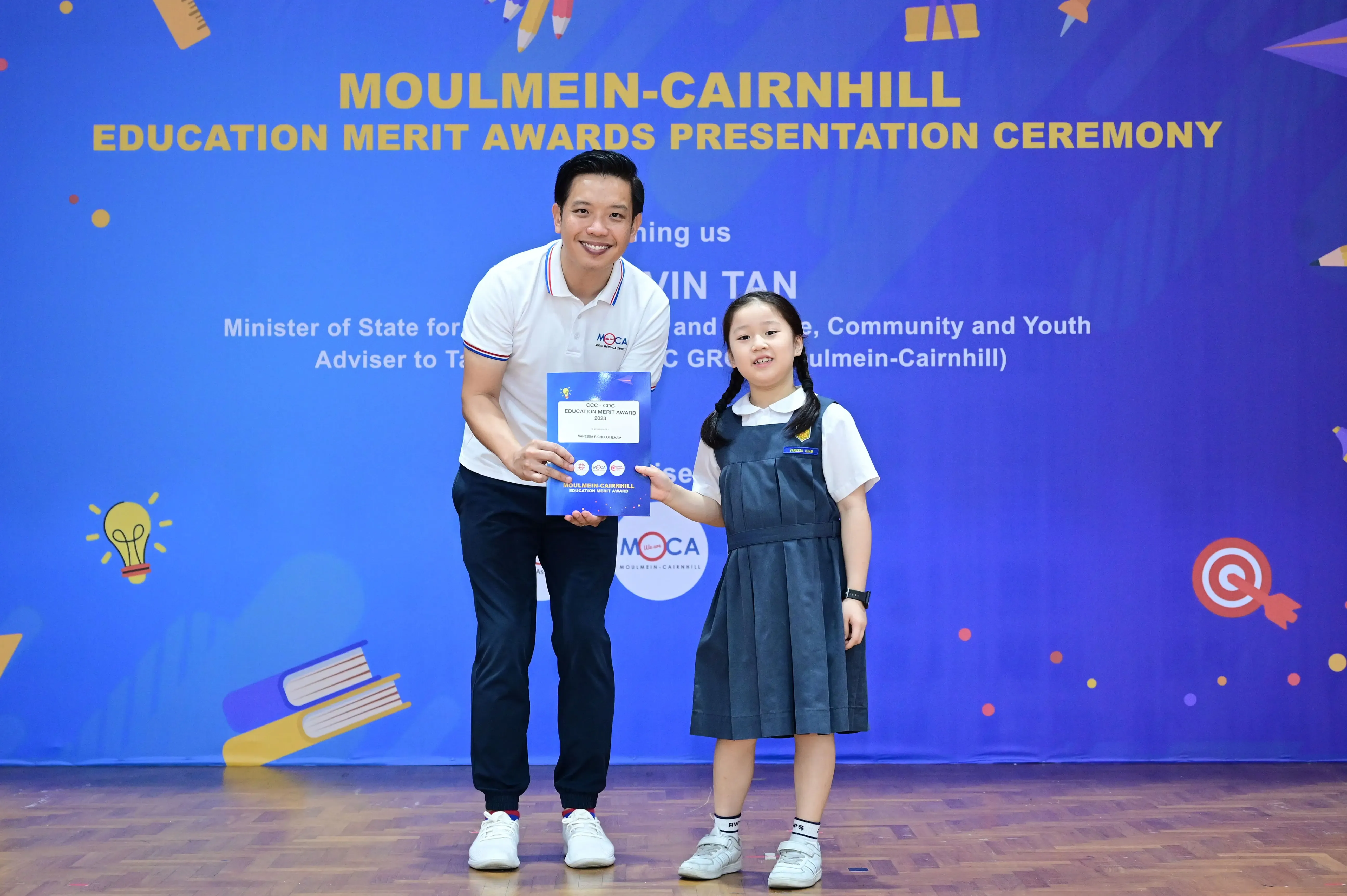 A man and a young girl in school uniform hold a certificate at the Moulmein-Cairnhill Education Merit Awards ceremony.