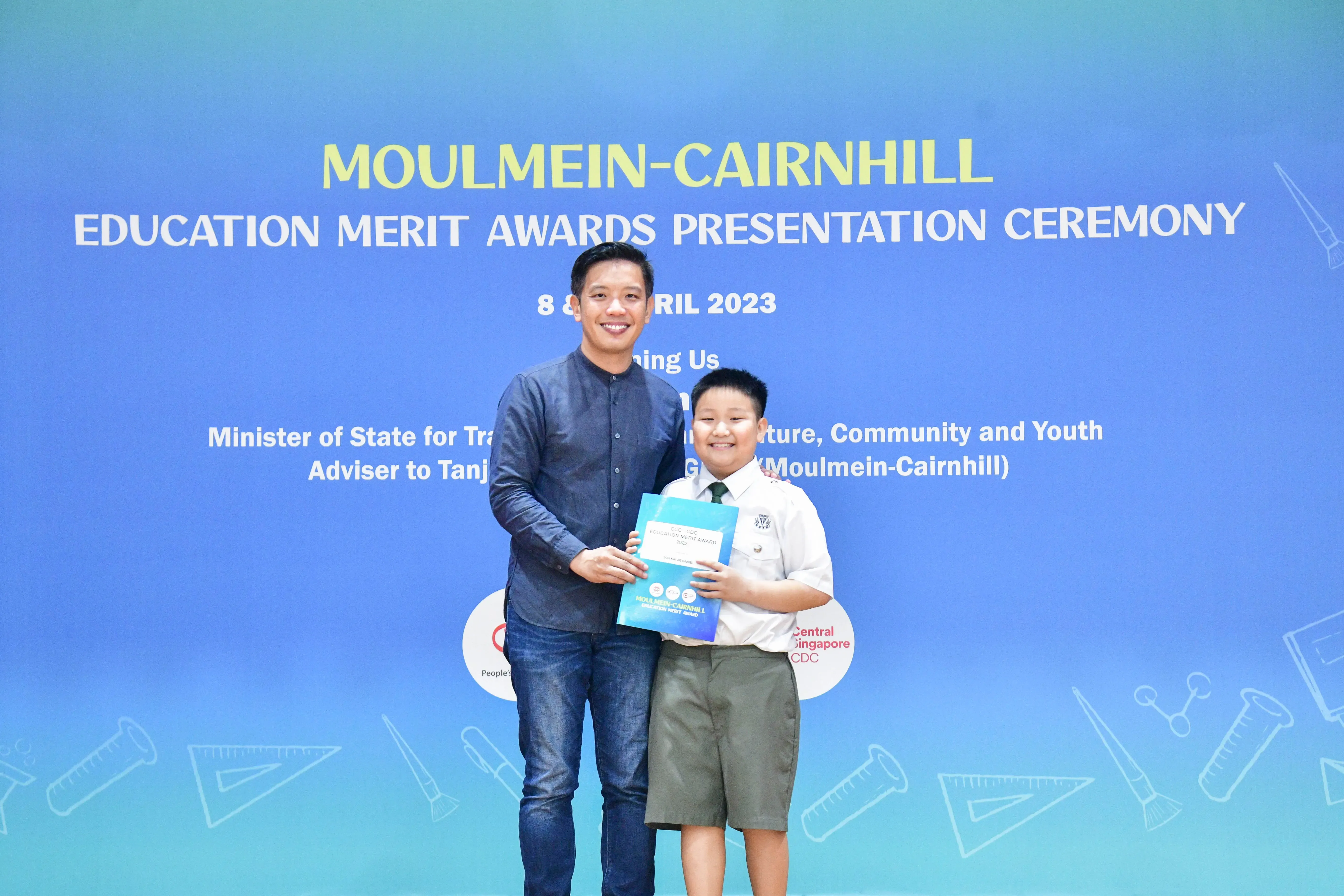 An adult and a young boy hold a certificate together at the Moulmein-Cairnhill Education Merit Awards 2023.