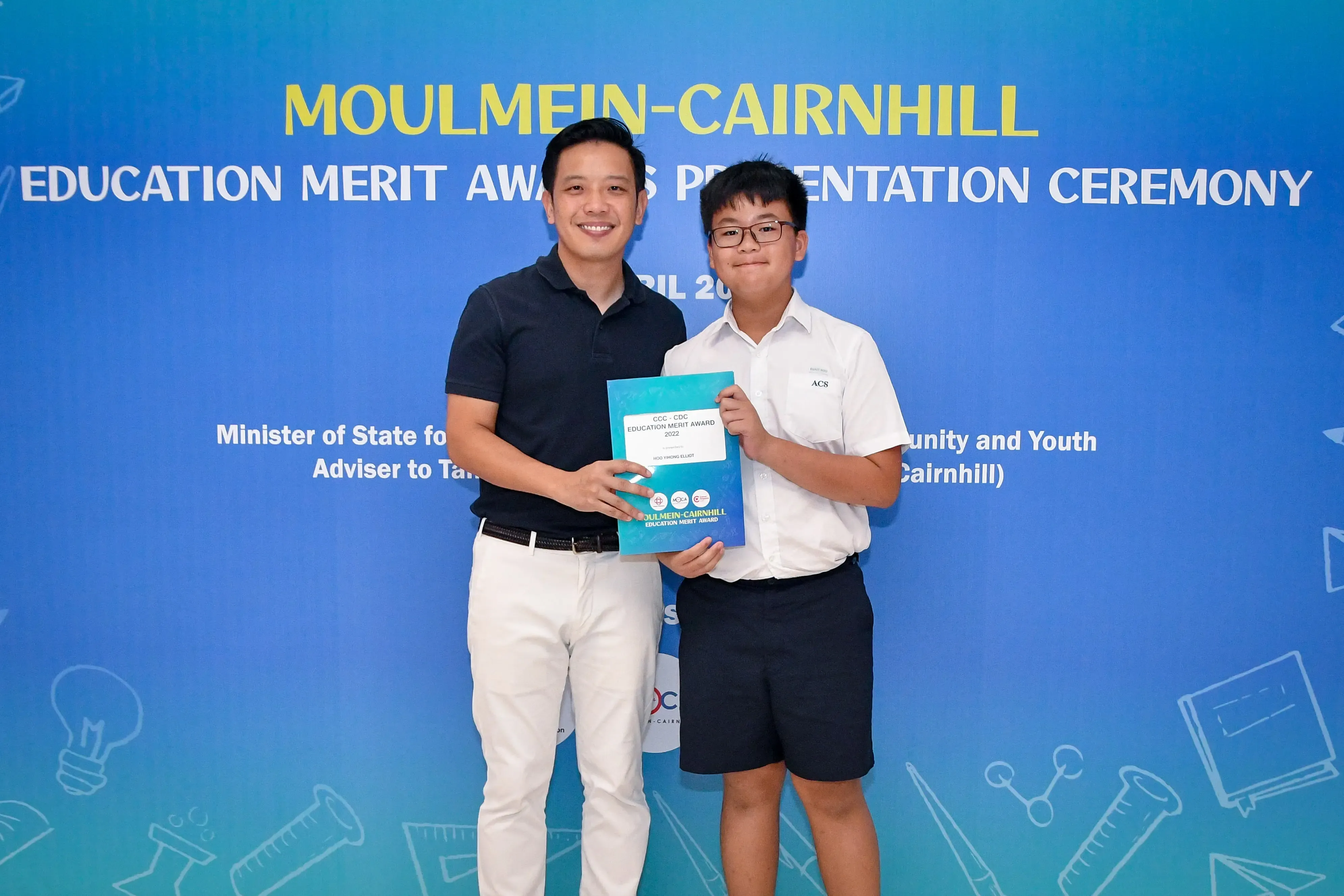 A man and a young student hold an award certificate at the Moulmein-Cairnhill Education Merit Awards Ceremony.