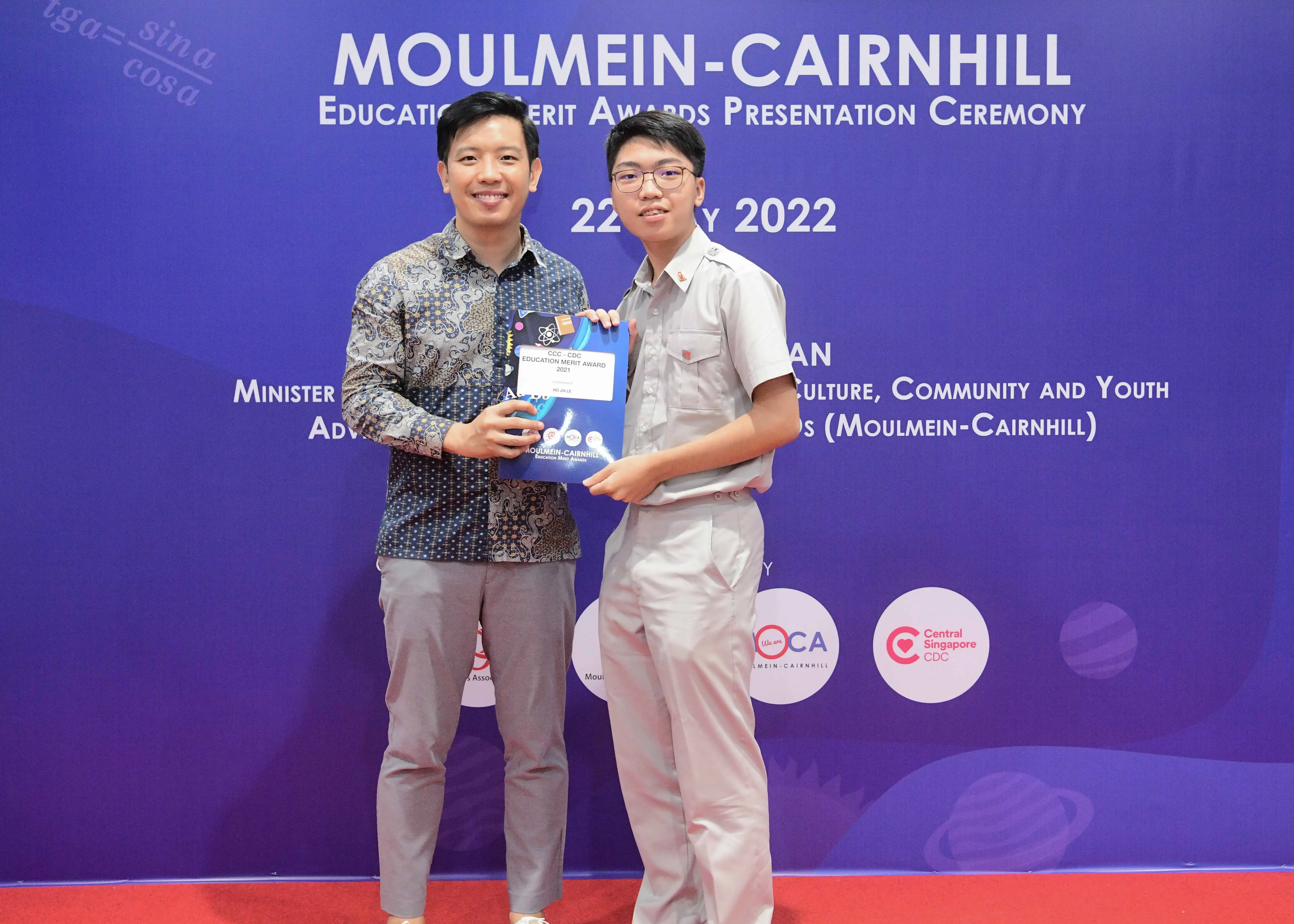 Two men smile holding an award certificate at the Moulmein-Cairnhill Education Merit Awards Ceremony, 2022.