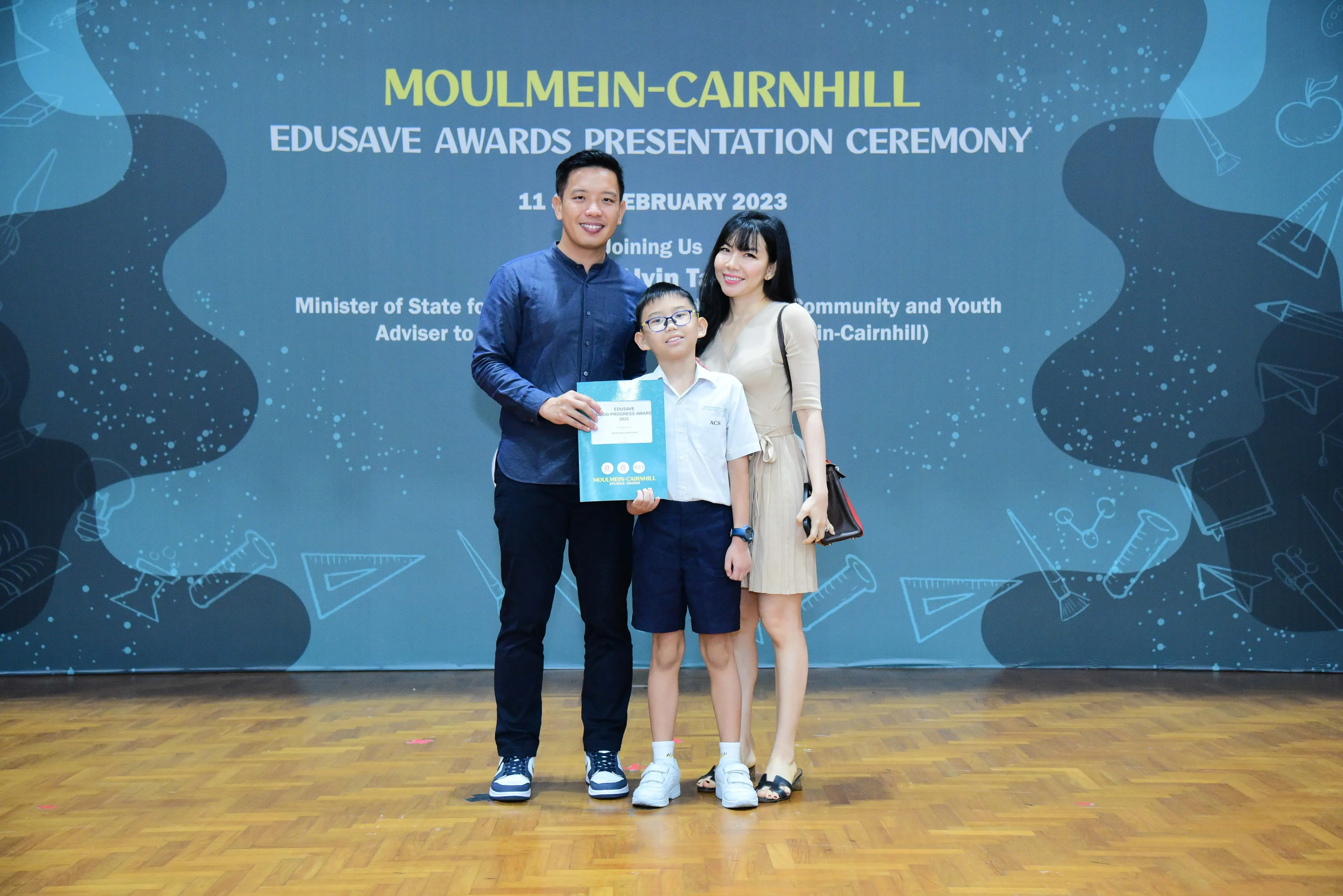 A man, boy holding a certificate, and woman pose at the Moulmein-Cairnhill Edusave Awards Ceremony on February 11, 2023.