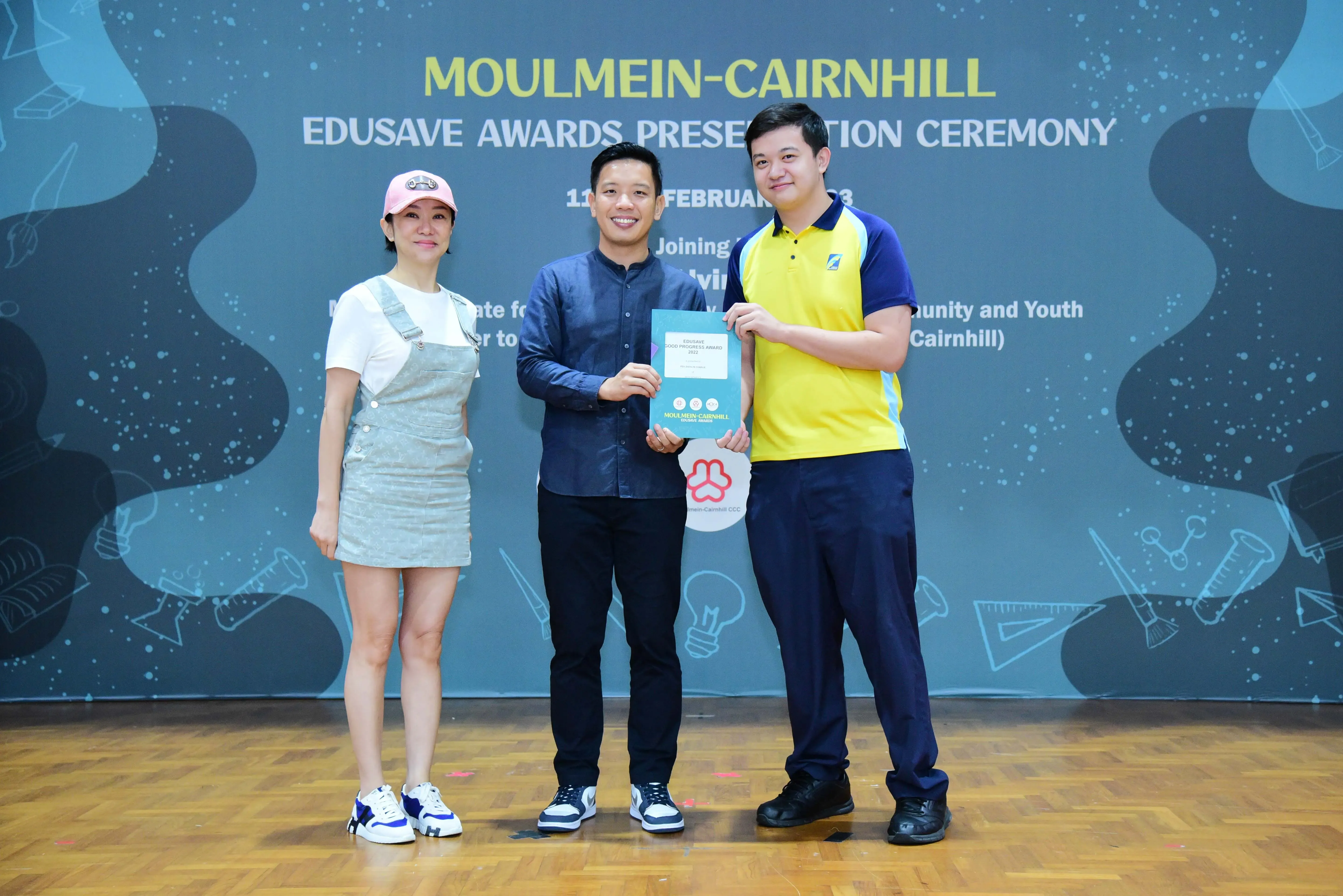 Three people pose smiling at the Moulmein-Cairnhill Edusave Awards Presentation Ceremony, with two holding a certificate.