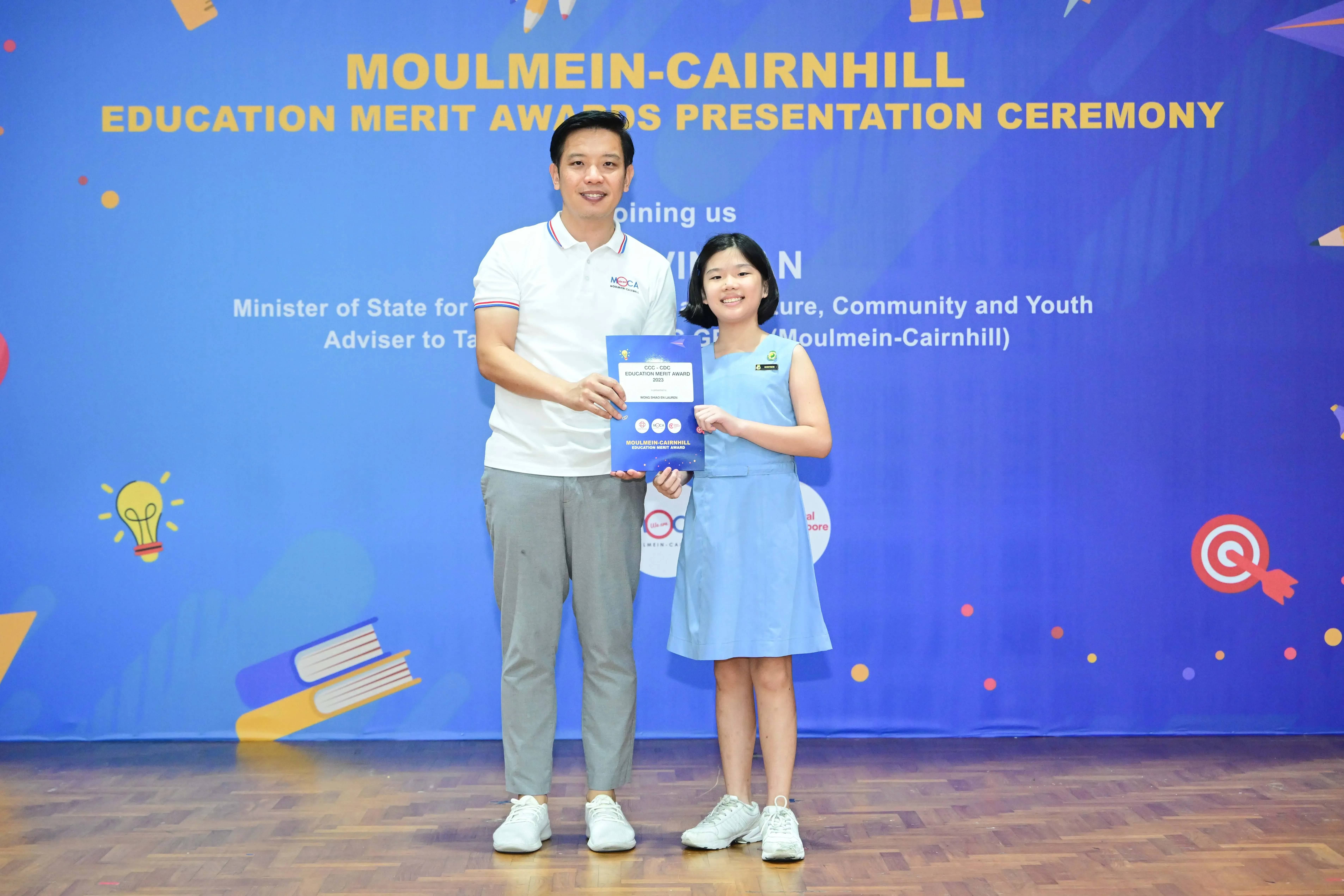 A man and a young girl hold a certificate together at the Moulmein-Cairnhill Education Merit Awards ceremony.
